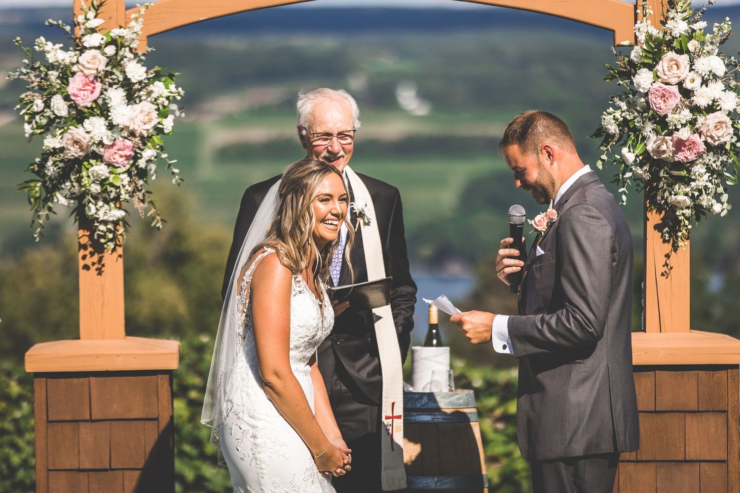 A joyful moment during an outdoor wedding ceremony under a floral arch with mountain views.