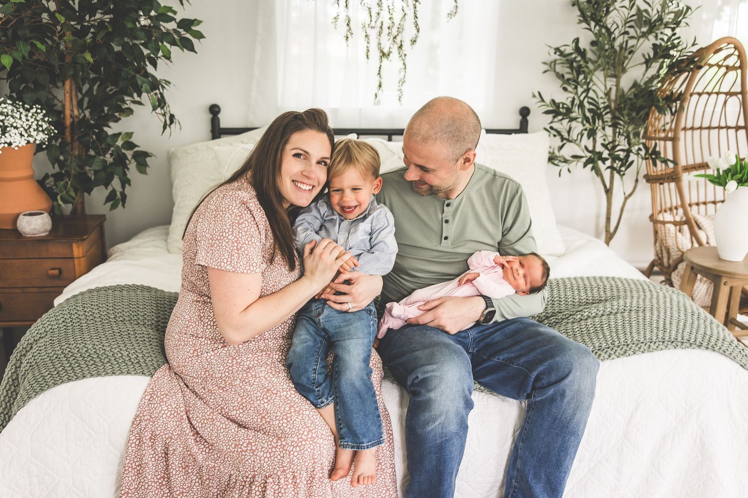A family shares intimate moments together on a white couch in a bright, plant-filled room.