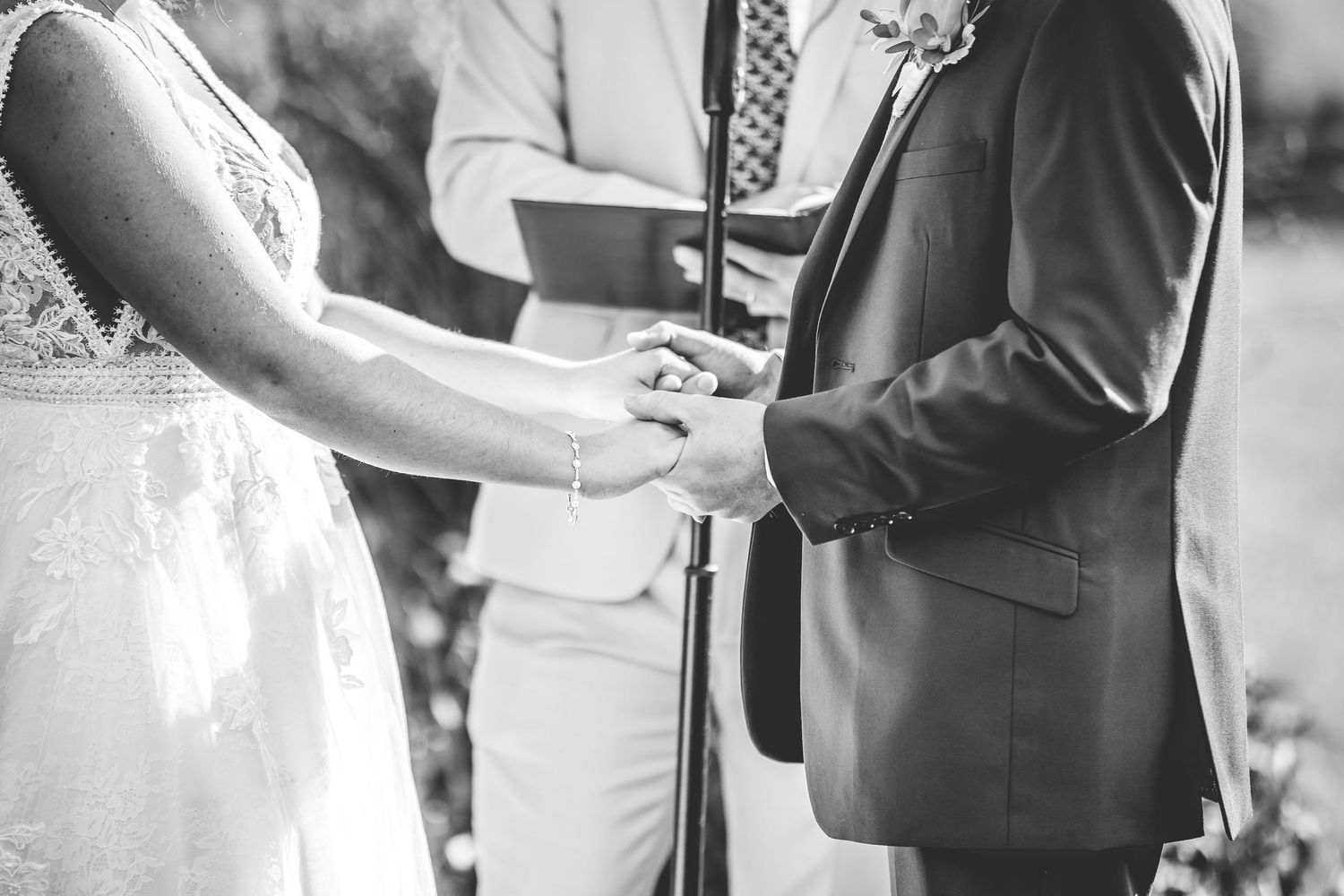 Close-up black and white photo of hands during ring exchange at wedding ceremony.