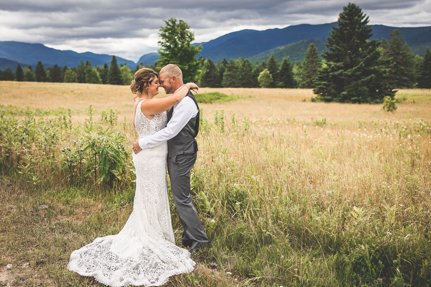 A couple shares an intimate moment on a scenic country road with mountains in the background.