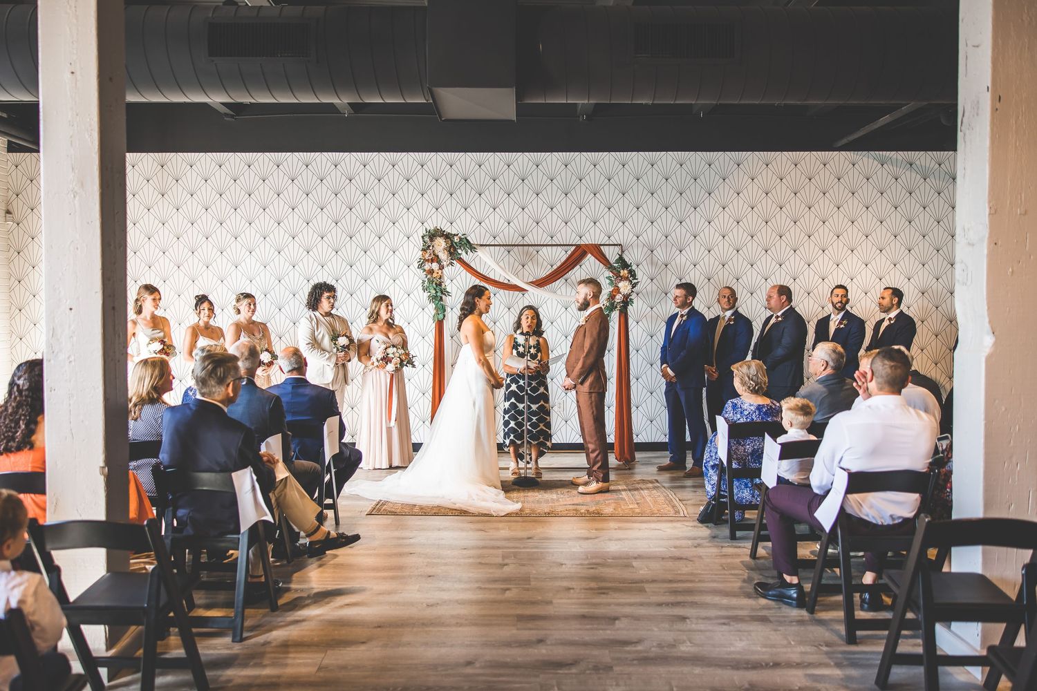 Wide view of wedding ceremony setup with geometric backdrop and rows of guest seating.