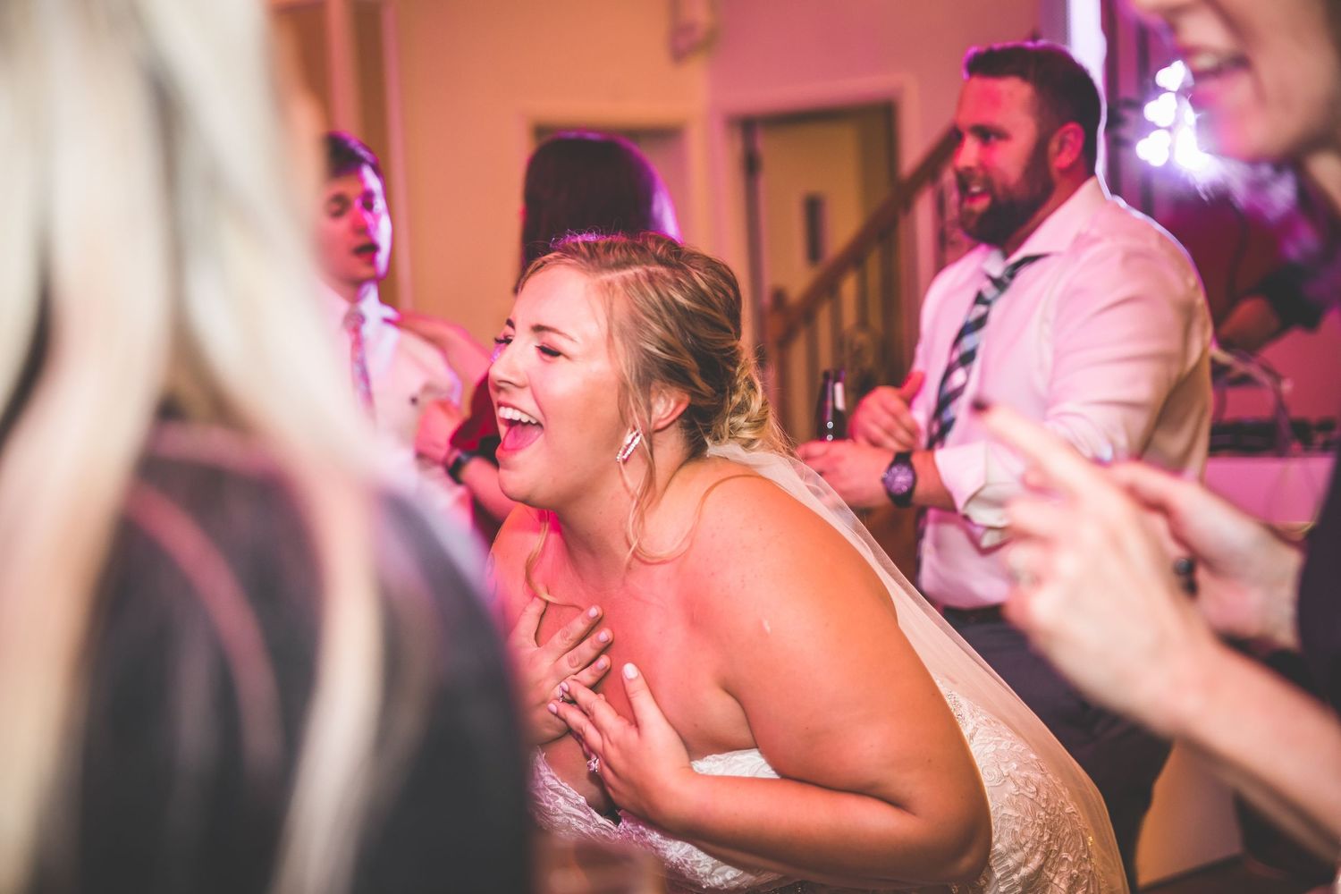 Wedding reception guests dancing and celebrating on a pink-lit dance floor.