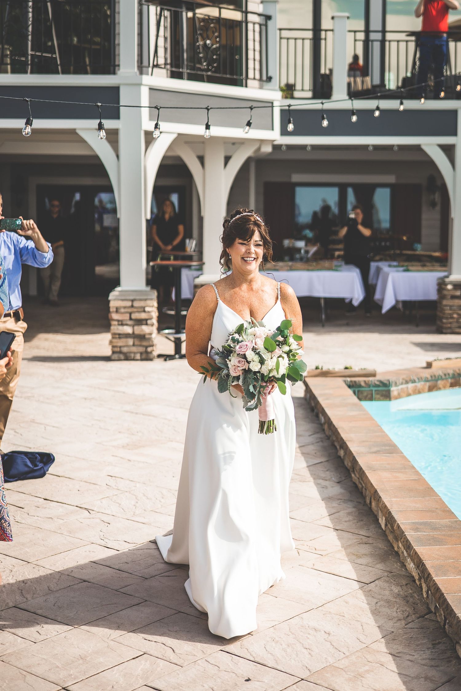Wedding ceremony setup by a poolside patio with white architectural details and stone columns.