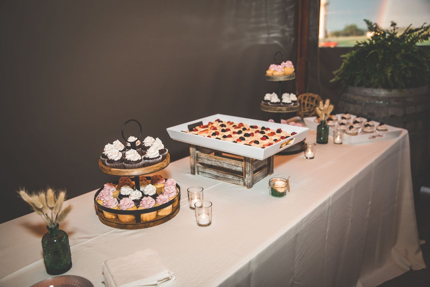Wedding dessert table with various cakes and treats displayed on white linens.