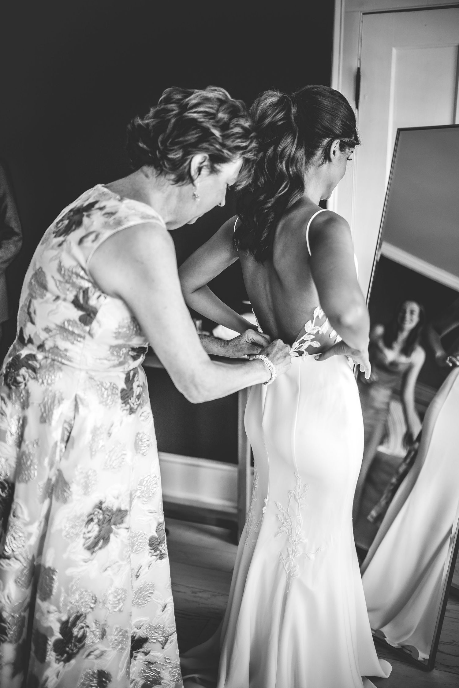 Bridesmaids in floral dresses help with wedding preparations in an elegant indoor setting.