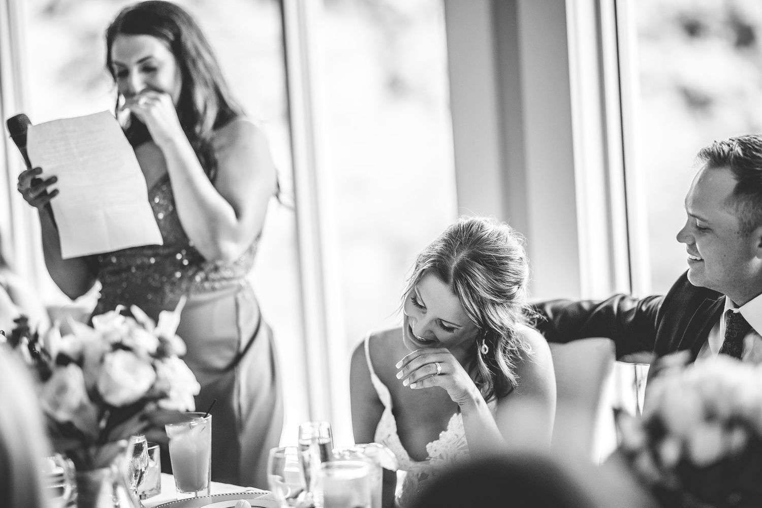 Black and white candid shots capture emotional reactions during wedding reception speeches.