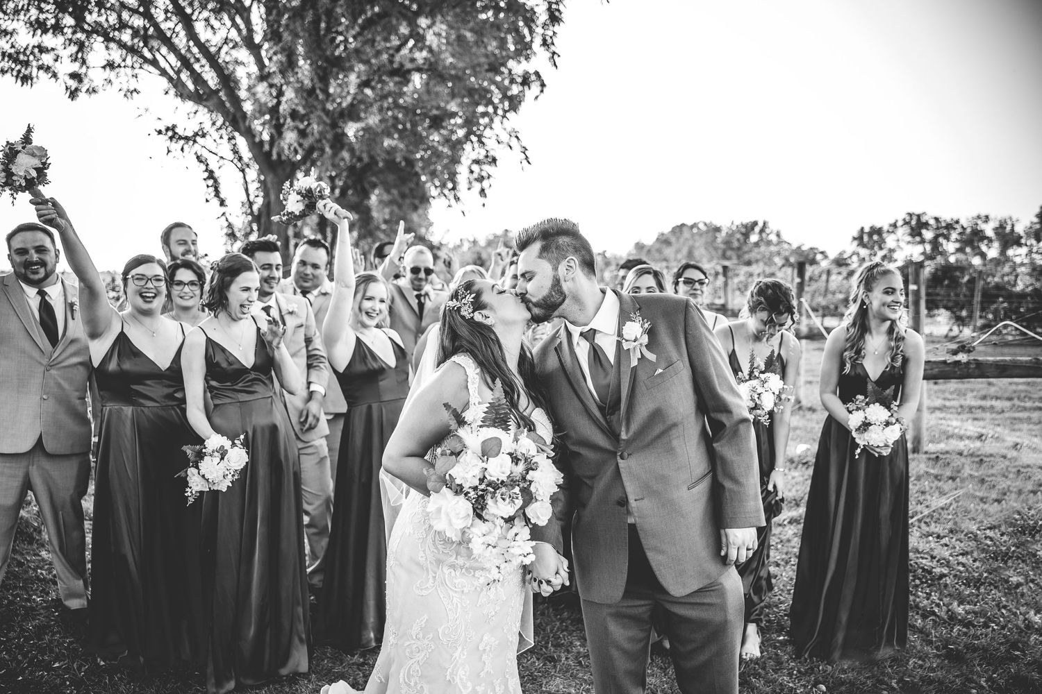 Black and white candid shots of wedding party celebrating outdoors under tree canopy.