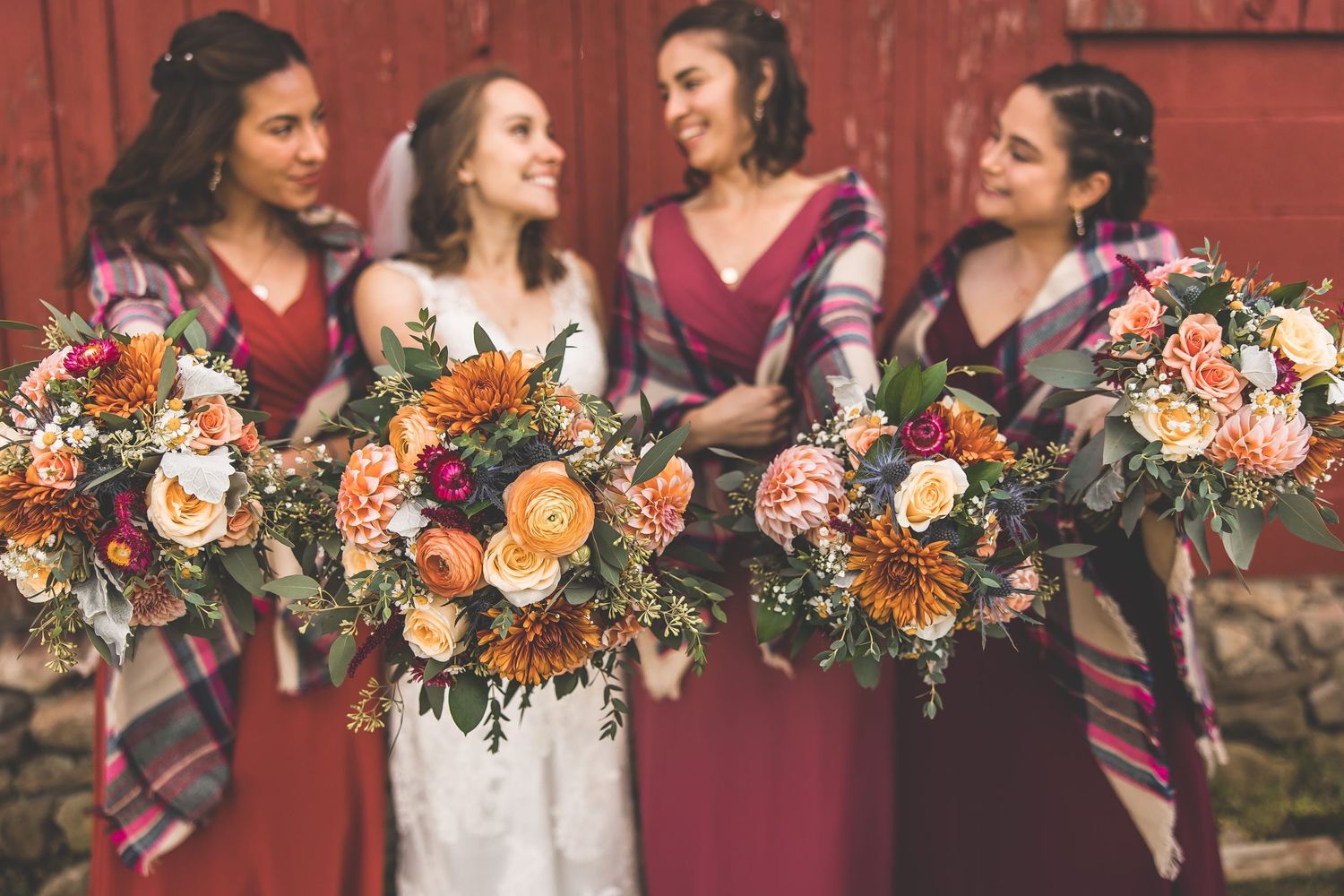 Wedding party holding vibrant orange and pink bouquets against rustic red barn backdrop.