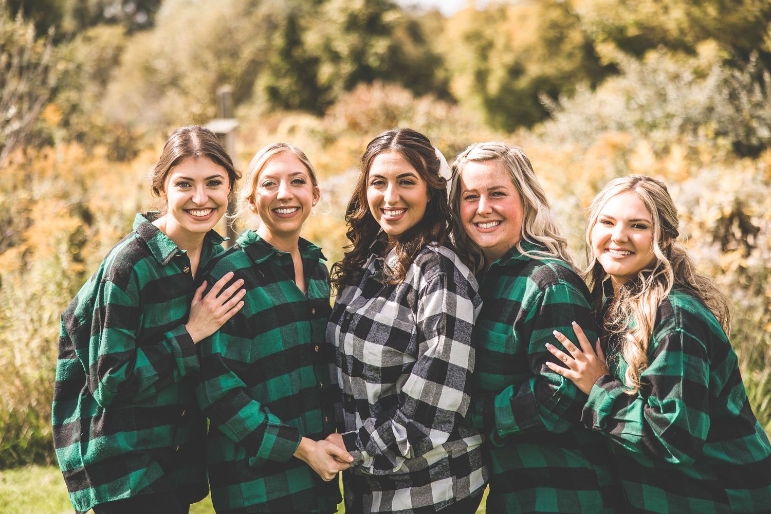 Friends wearing matching green and black buffalo plaid shirts laugh together outdoors.