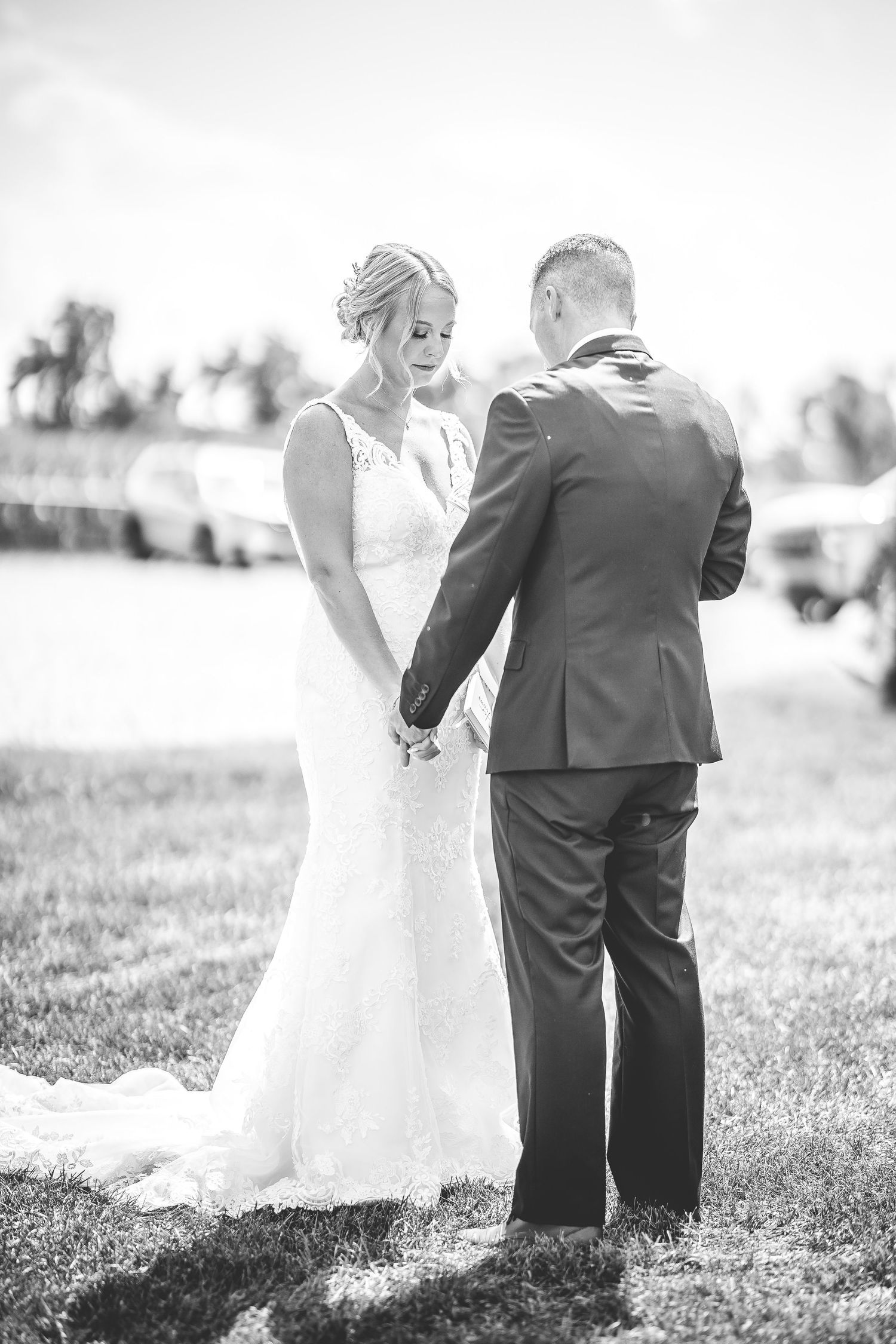 Black and white wedding photo showing a couple walking together through a sunlit garden.