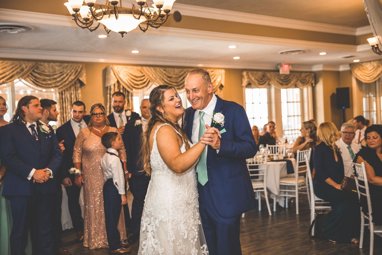 Wedding celebration in a grand ballroom with ornate window treatments and chandeliers.