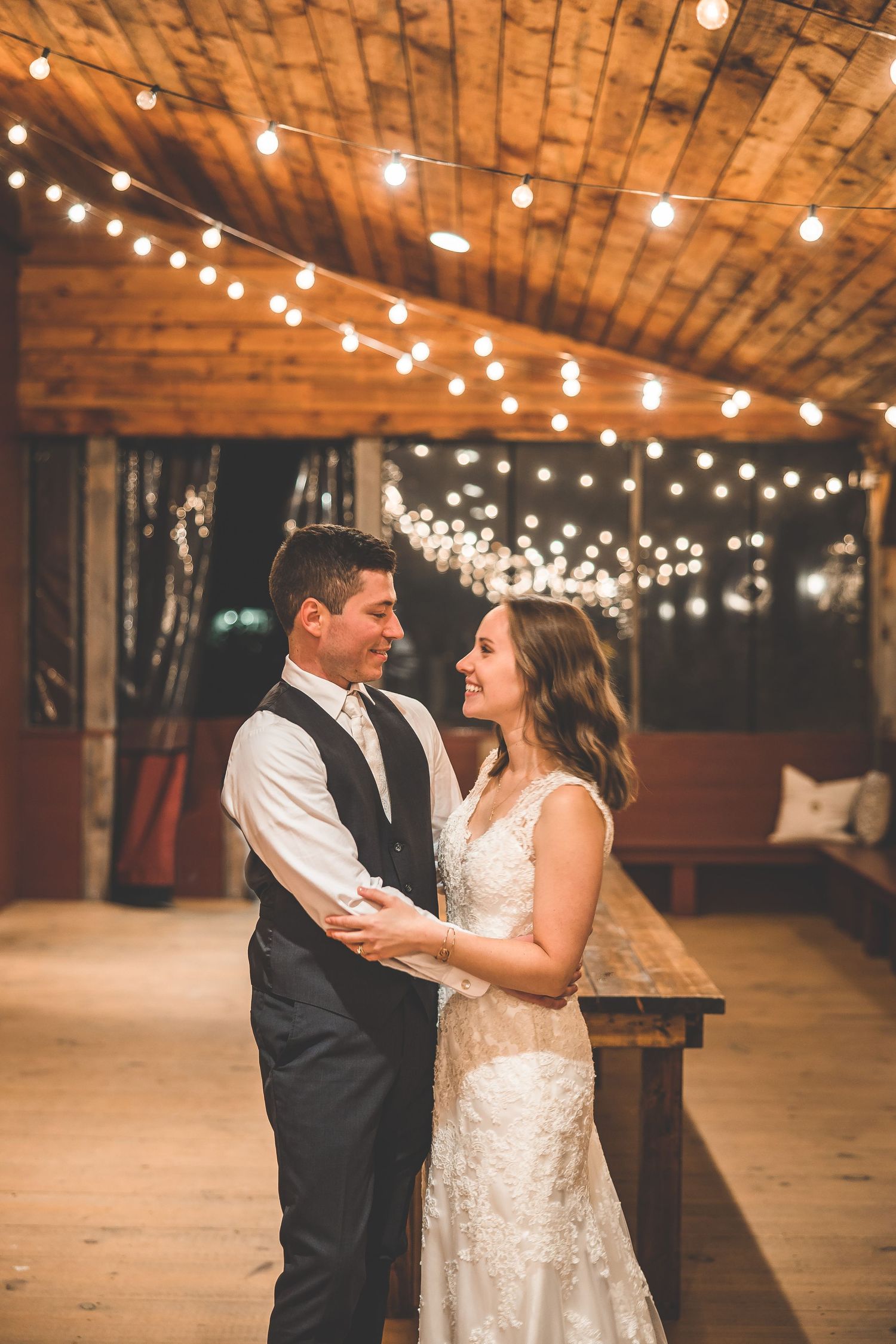 Newlyweds dance together in a rustic barn venue illuminated by warm string lights.