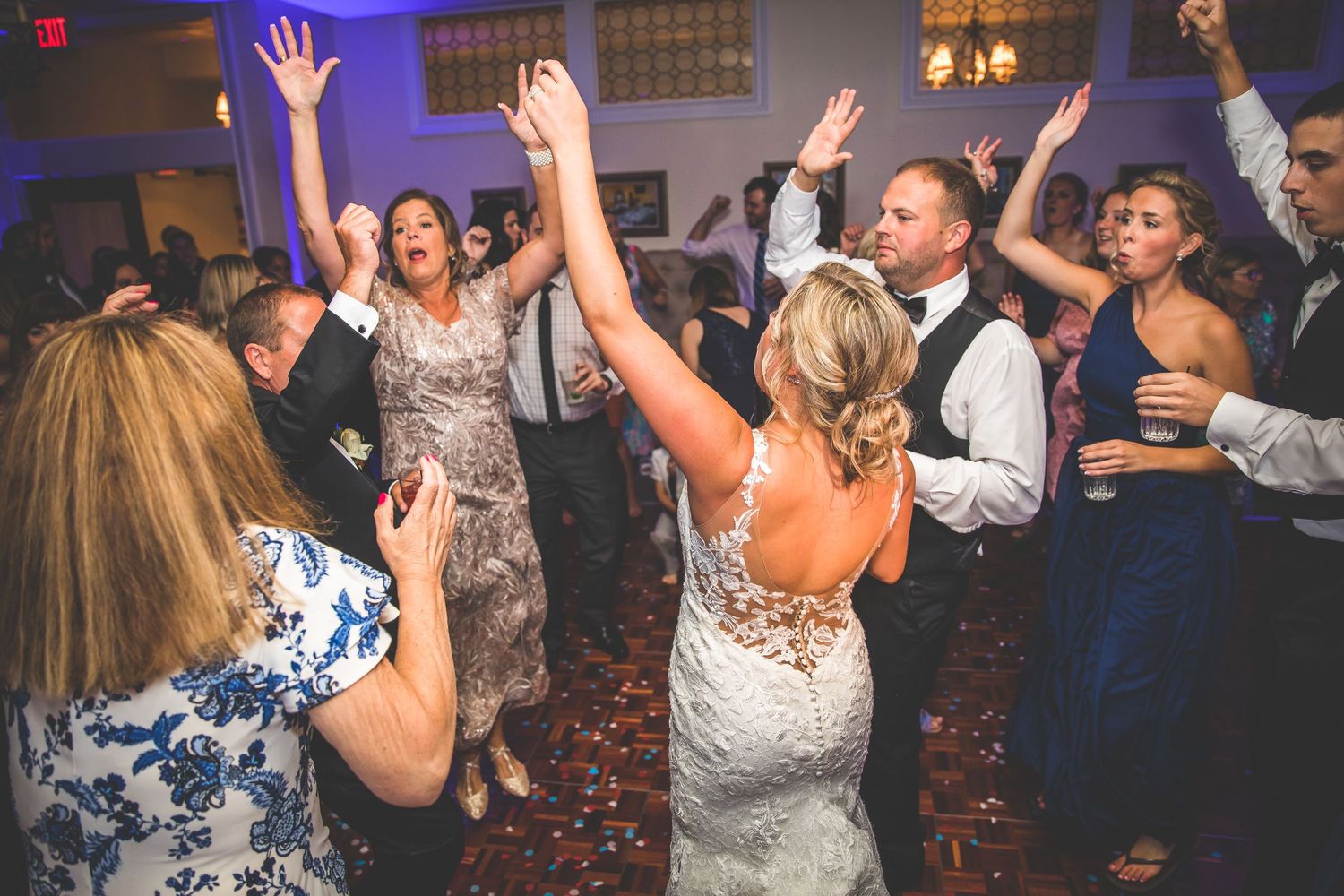 Wedding reception dance floor filled with guests dancing with hands raised in celebration.