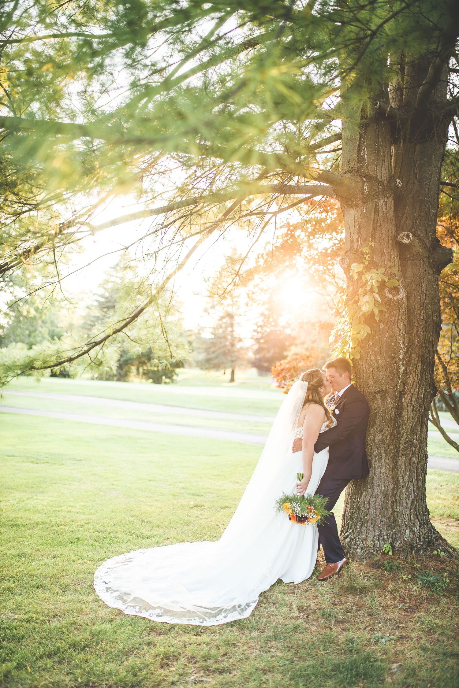 Romantic sunset wedding photos under large tree with flowing white dress and golden light.