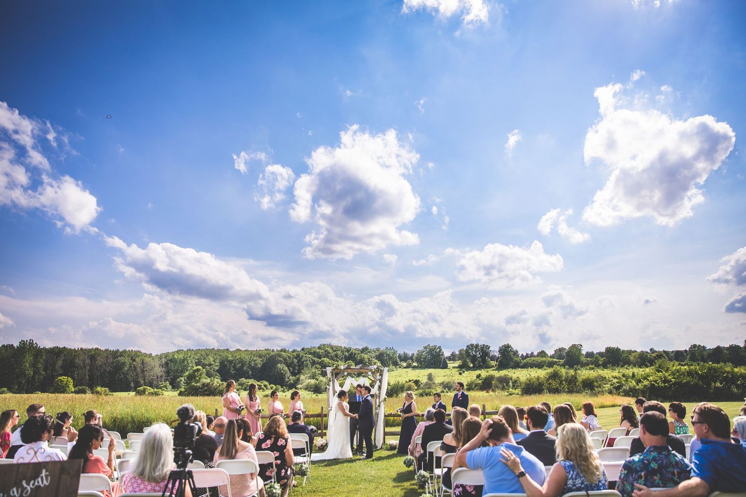 Wide angle view of wedding guests seated for an outdoor ceremony under blue summer skies.