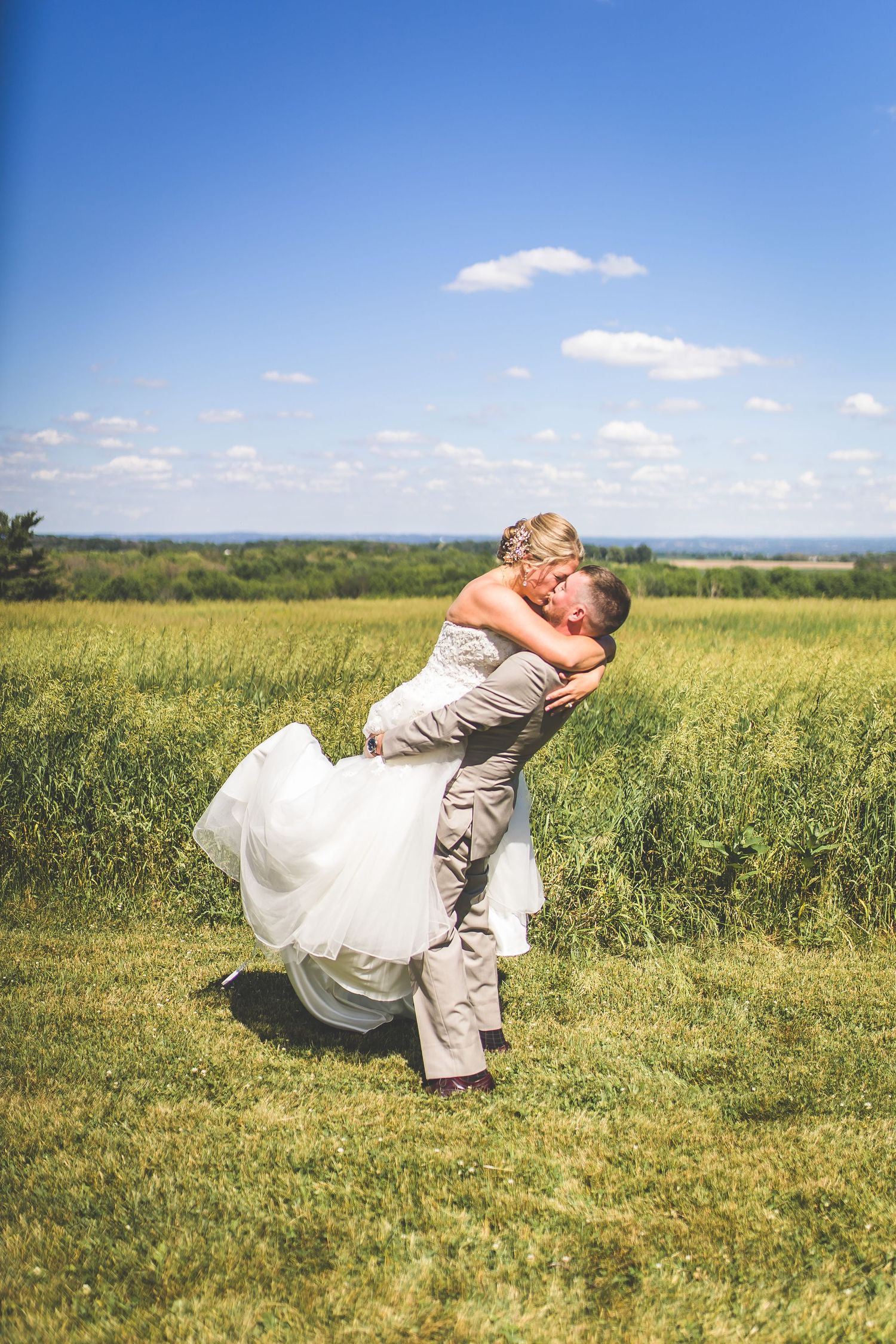 Wedding couple poses dramatically in a sunny yellow field with blue sky overhead.
