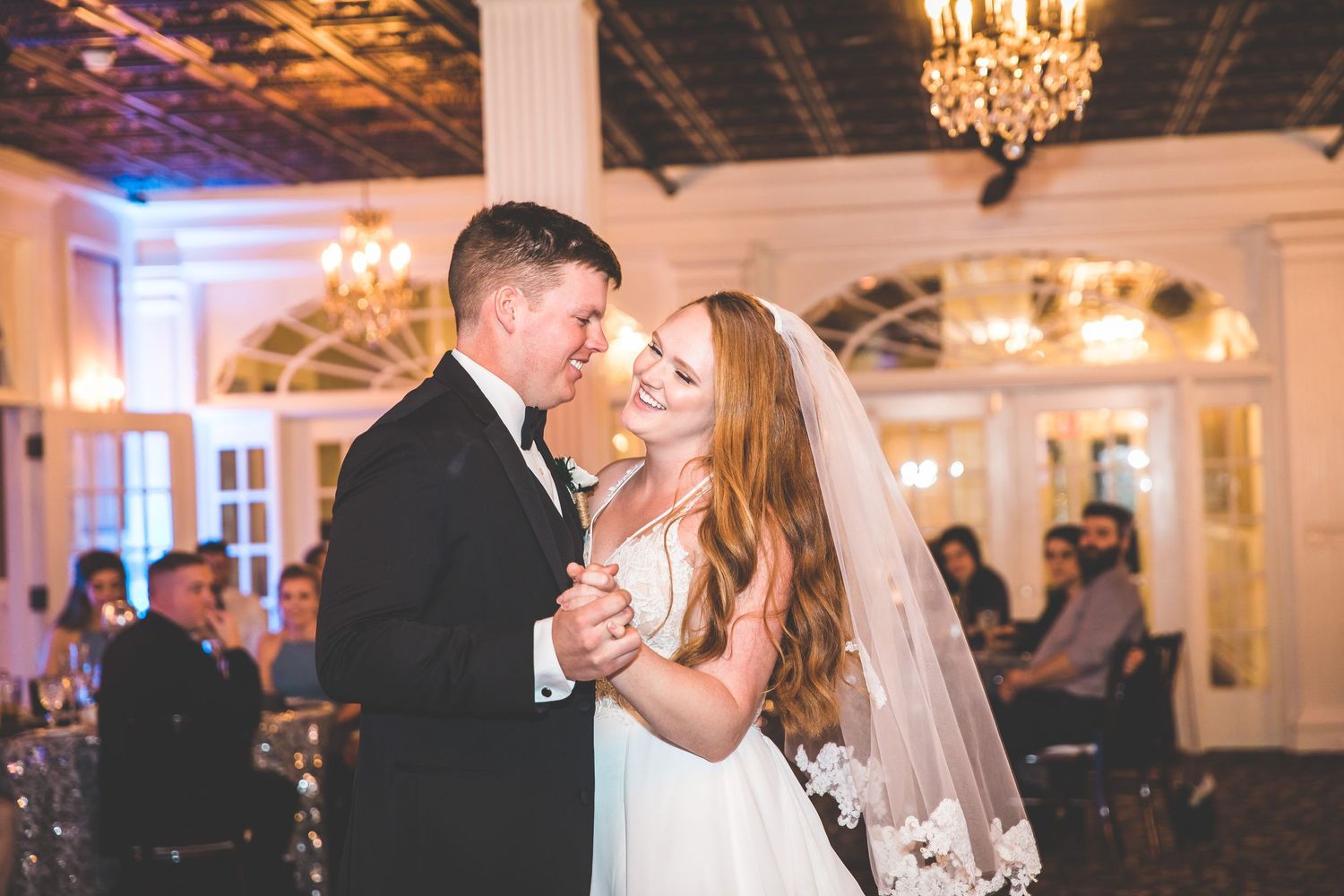 Wedding celebration in an elegant ballroom with crystal chandeliers and decorative ceiling.