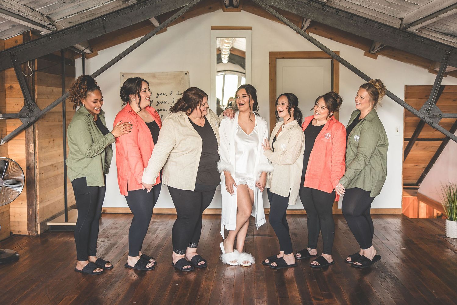Wedding party poses playfully in matching outfits inside rustic wooden venue.