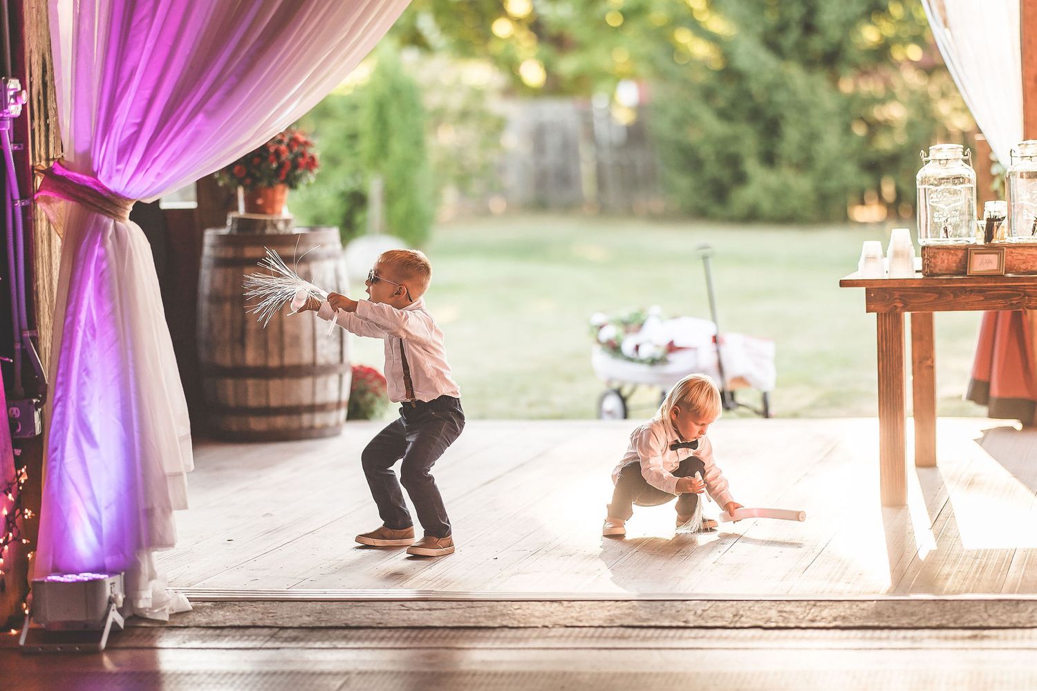 Children play under purple drapery at rustic barn wedding venue.