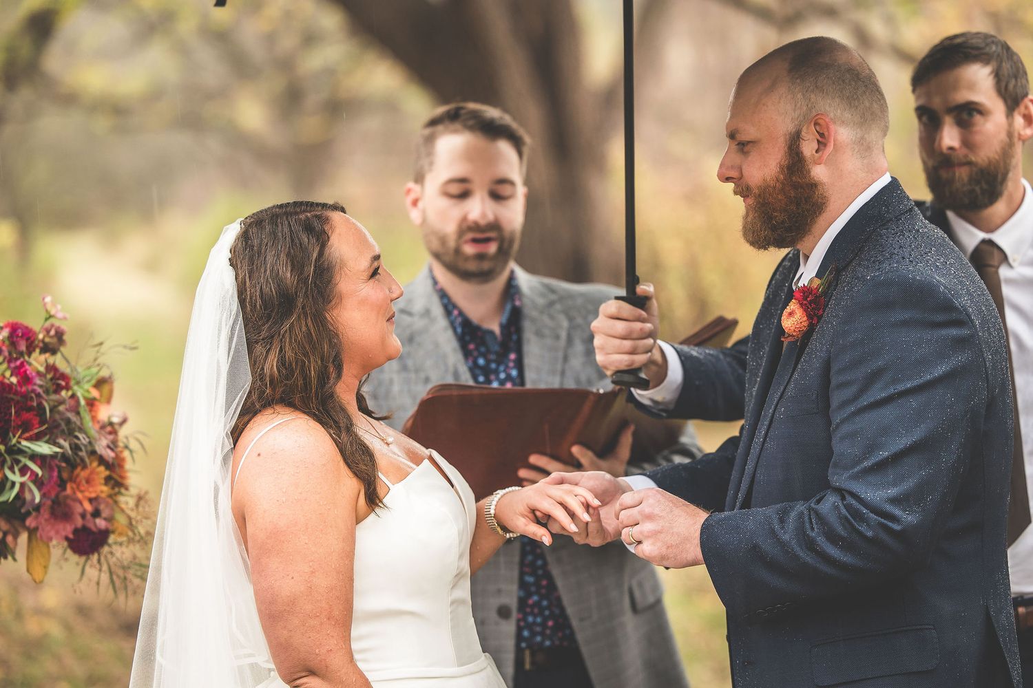 Close up of ring exchange during outdoor wedding ceremony with bridal party watching.