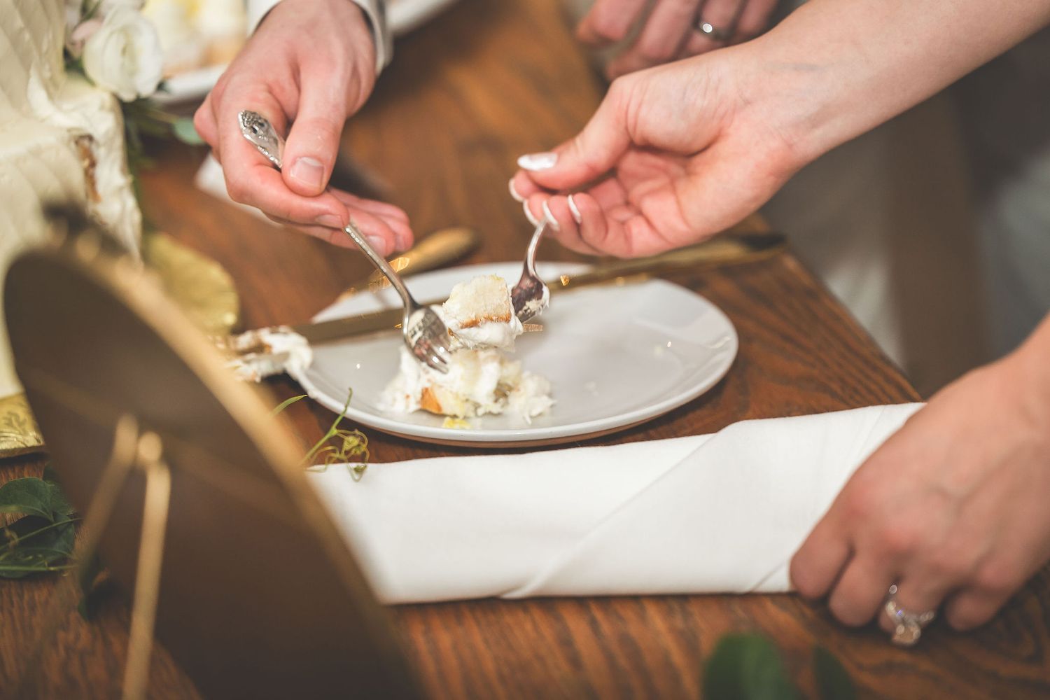 Close-up of hands cutting and serving wedding cake on white plates.