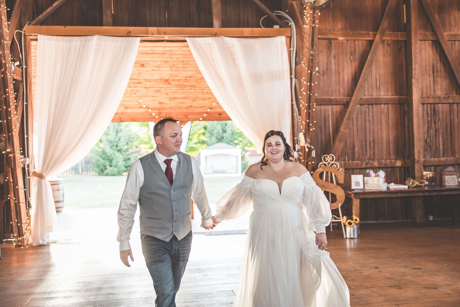 Wedding reception dance in a beautifully decorated rustic barn with white fabric draping and wooden beams.