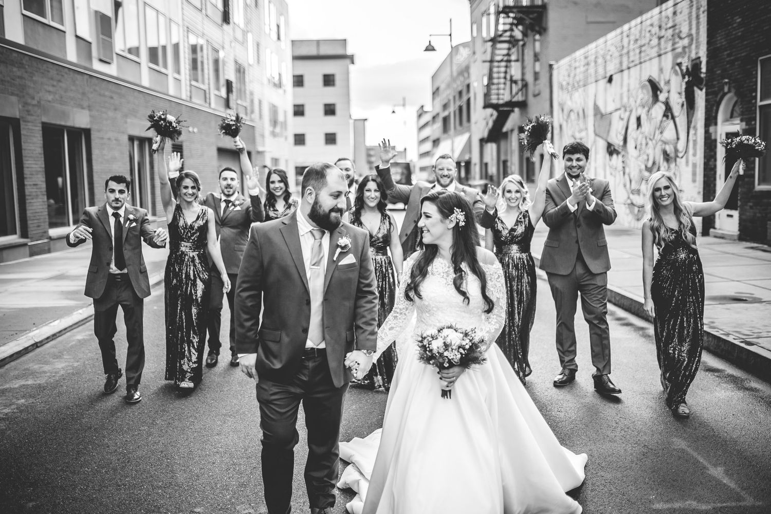 Black and white photo of wedding party walking down city street in formal attire.