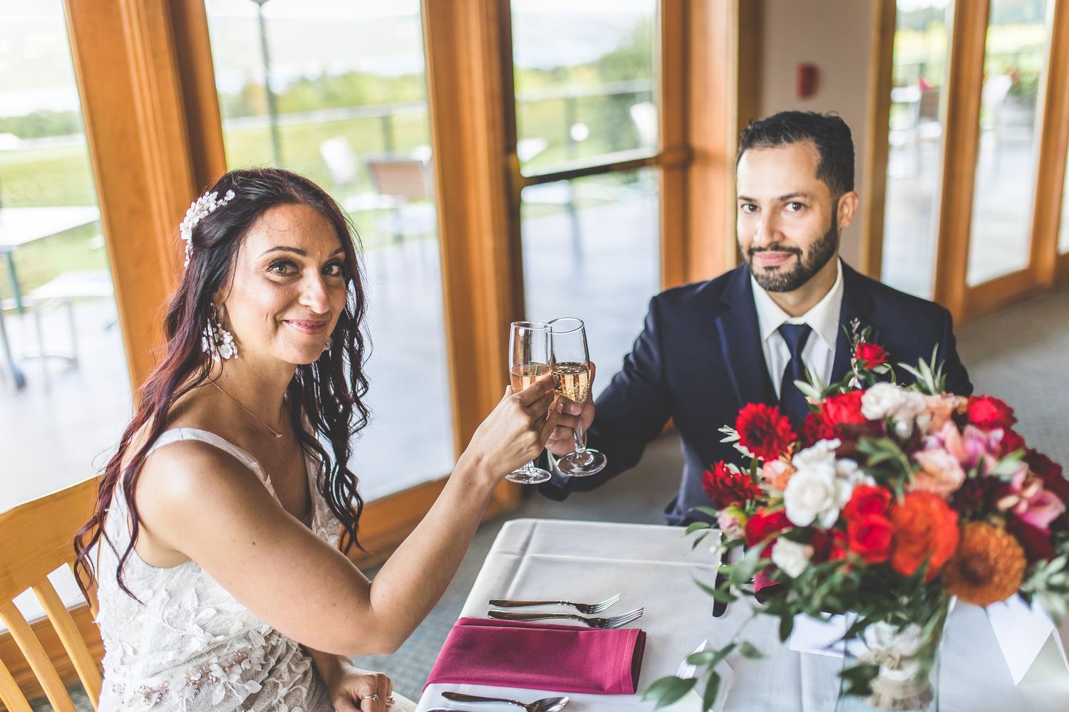 Reception table settings with red floral centerpieces in rustic wooden venue.