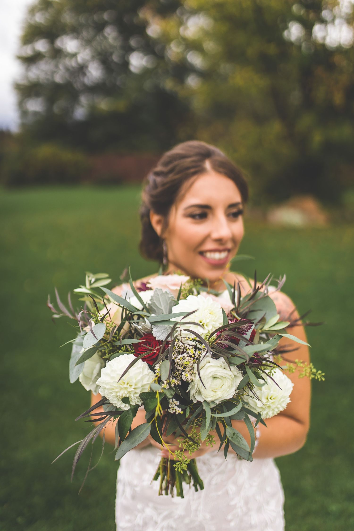 Close-up of bridal bouquet featuring white flowers and greenery against wedding dress.