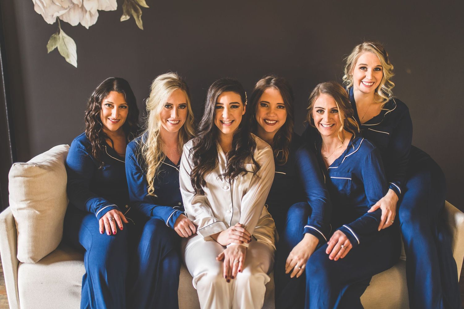 Bridesmaids in royal blue dresses pose together on a dark background for wedding photos.