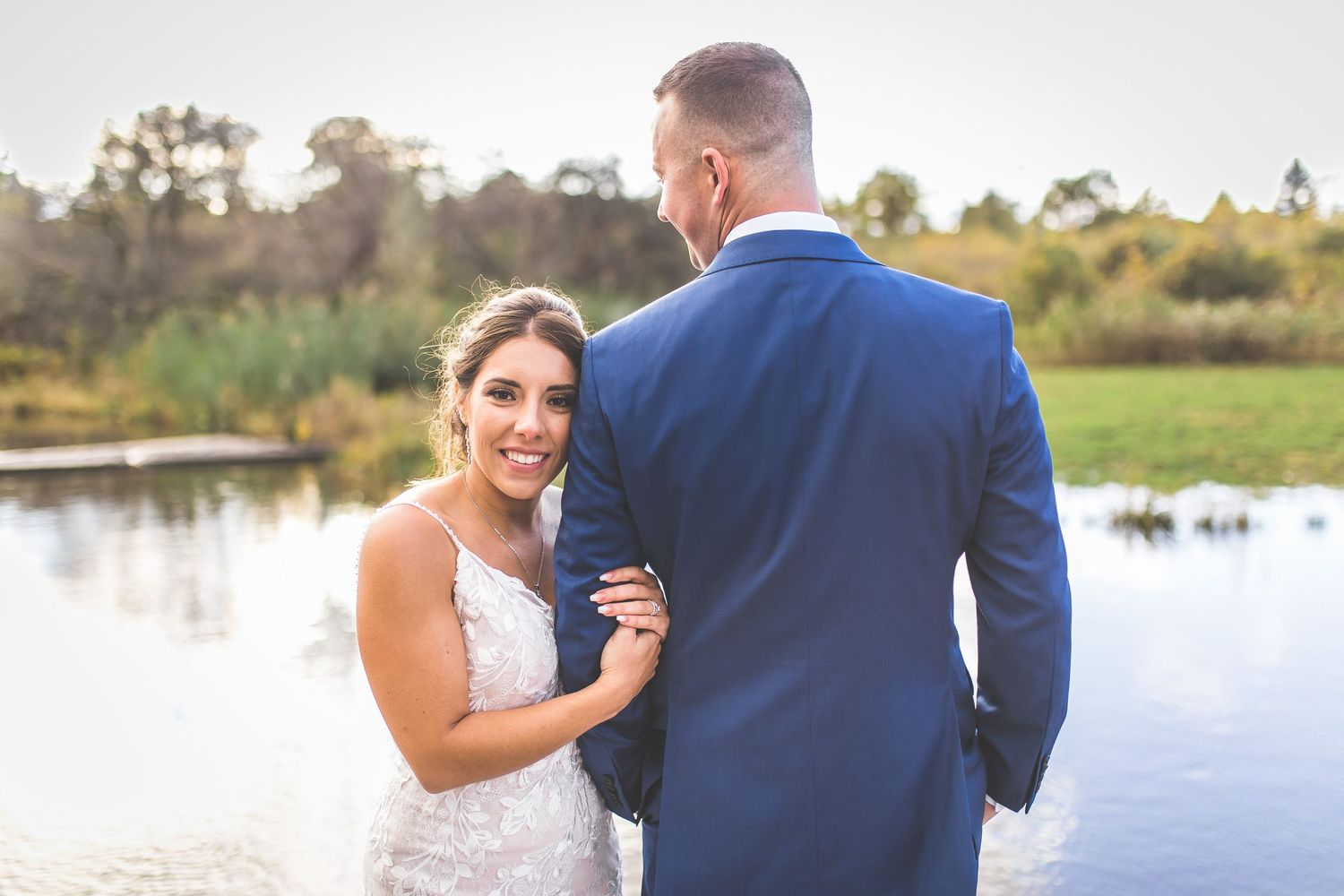 Wedding couple poses together on wooden pier with water and nature in background.