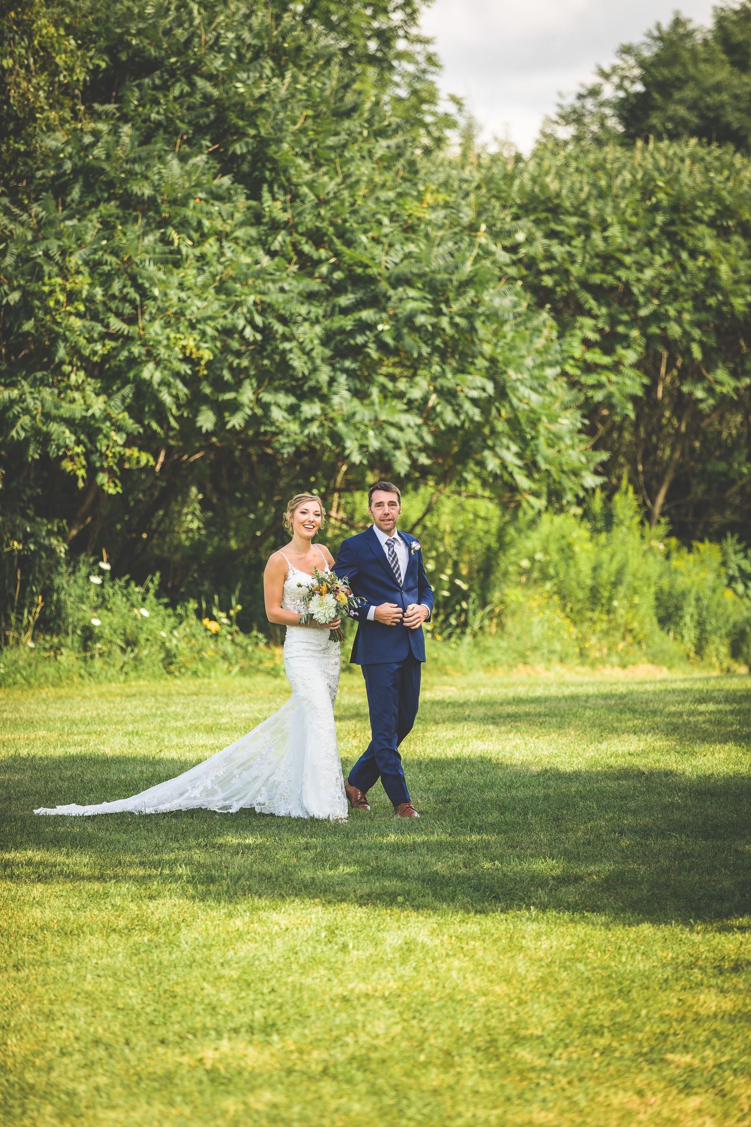 A couple walks together on lush green grass during their outdoor wedding celebration.