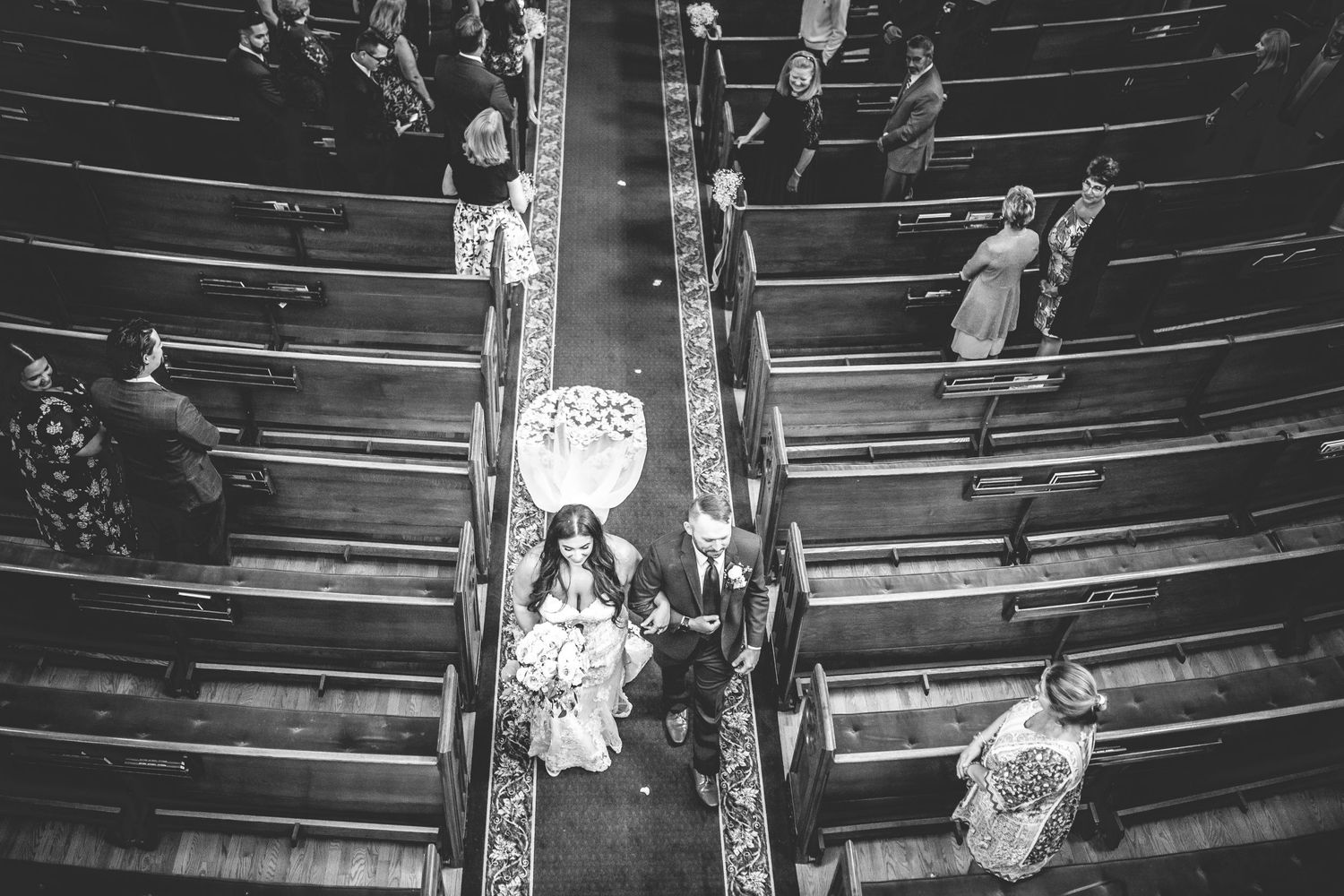 Overhead view of wedding guests seated in wooden church pews during a ceremony.