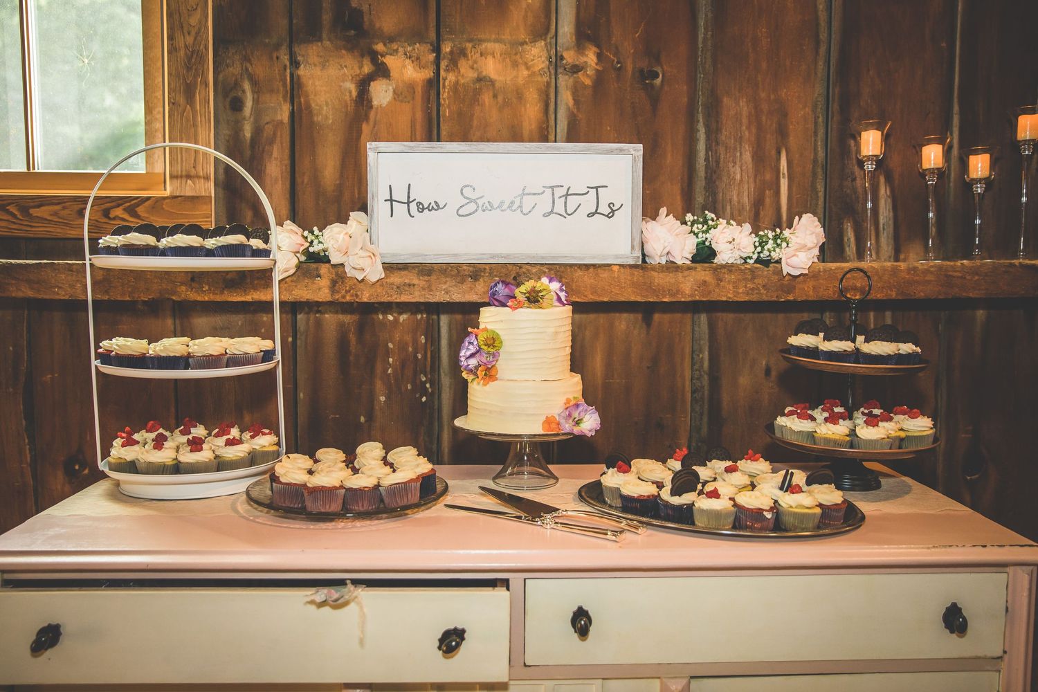 Rustic dessert table display with cupcakes and treats at a barn wedding reception.