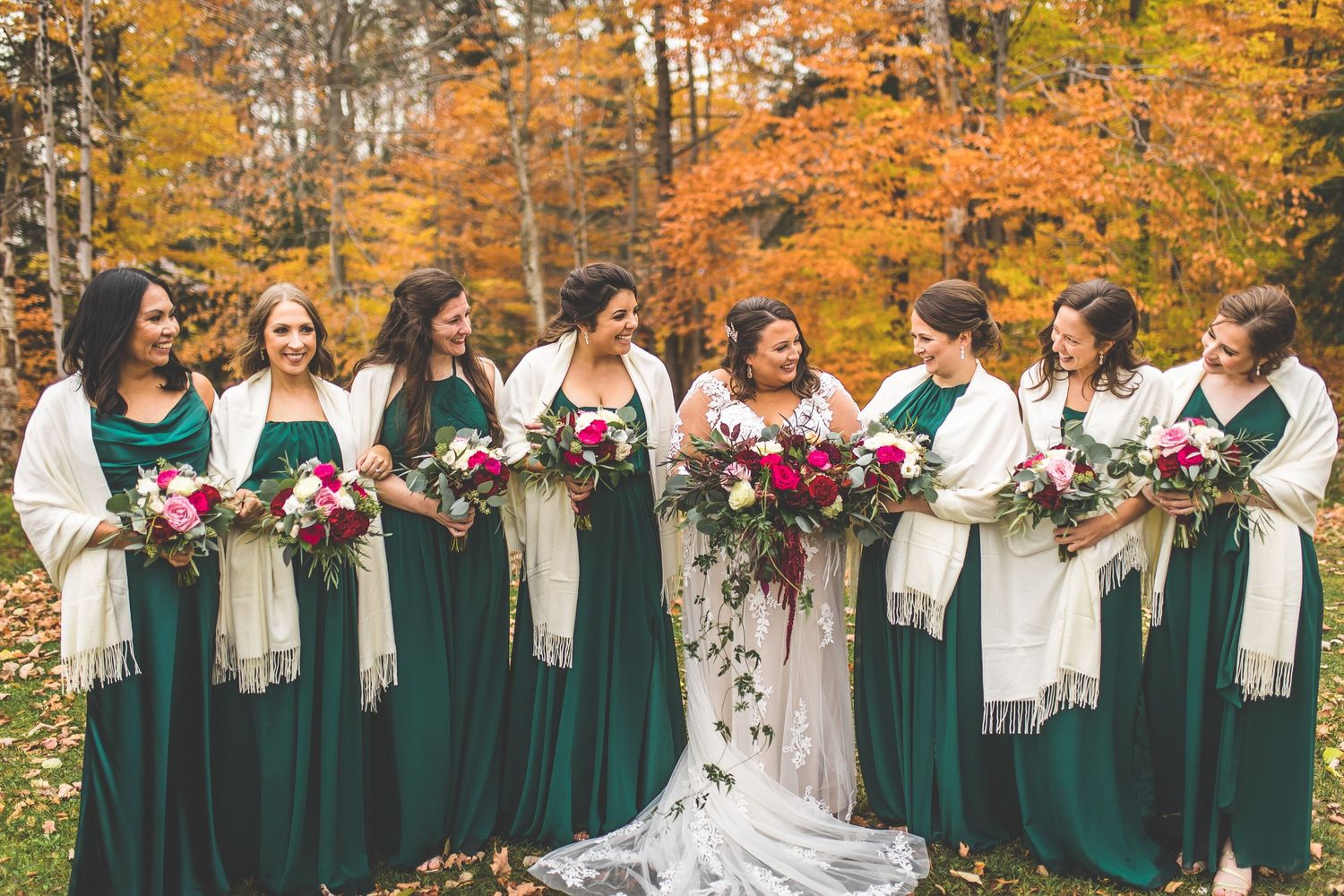 Bridesmaids in emerald green dresses pose against a backdrop of fall colors.