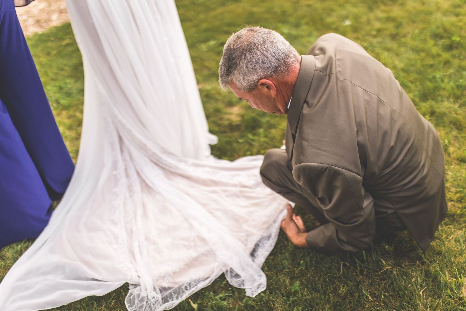 Close-up details of white lace wedding dress train spread out on green grass.