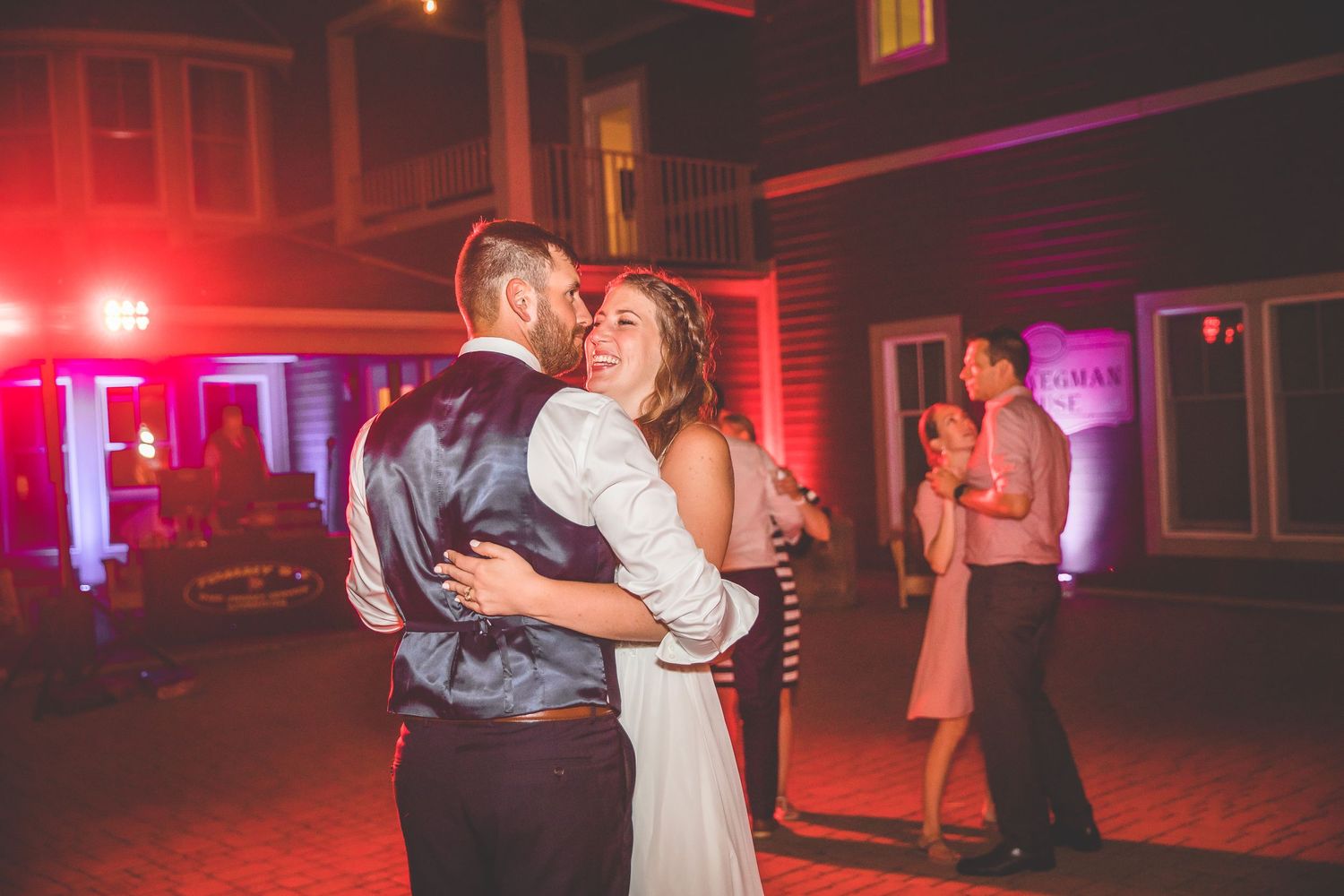 Couples dance under red mood lighting at an evening wedding reception.