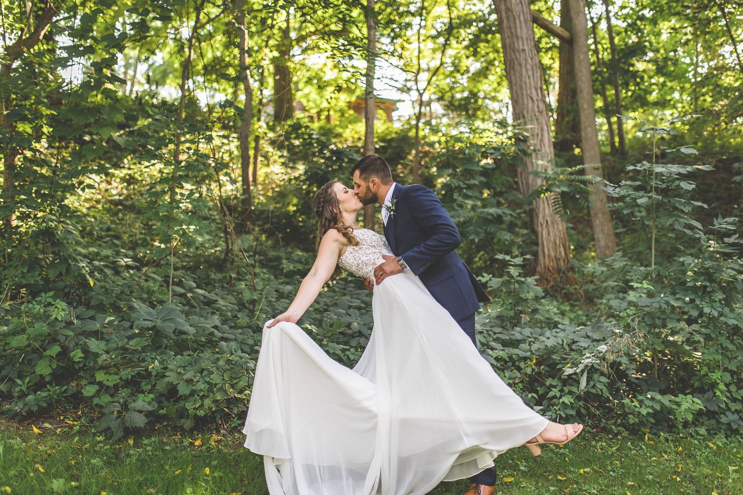 A couple shares a romantic dance pose in a lush green garden setting.