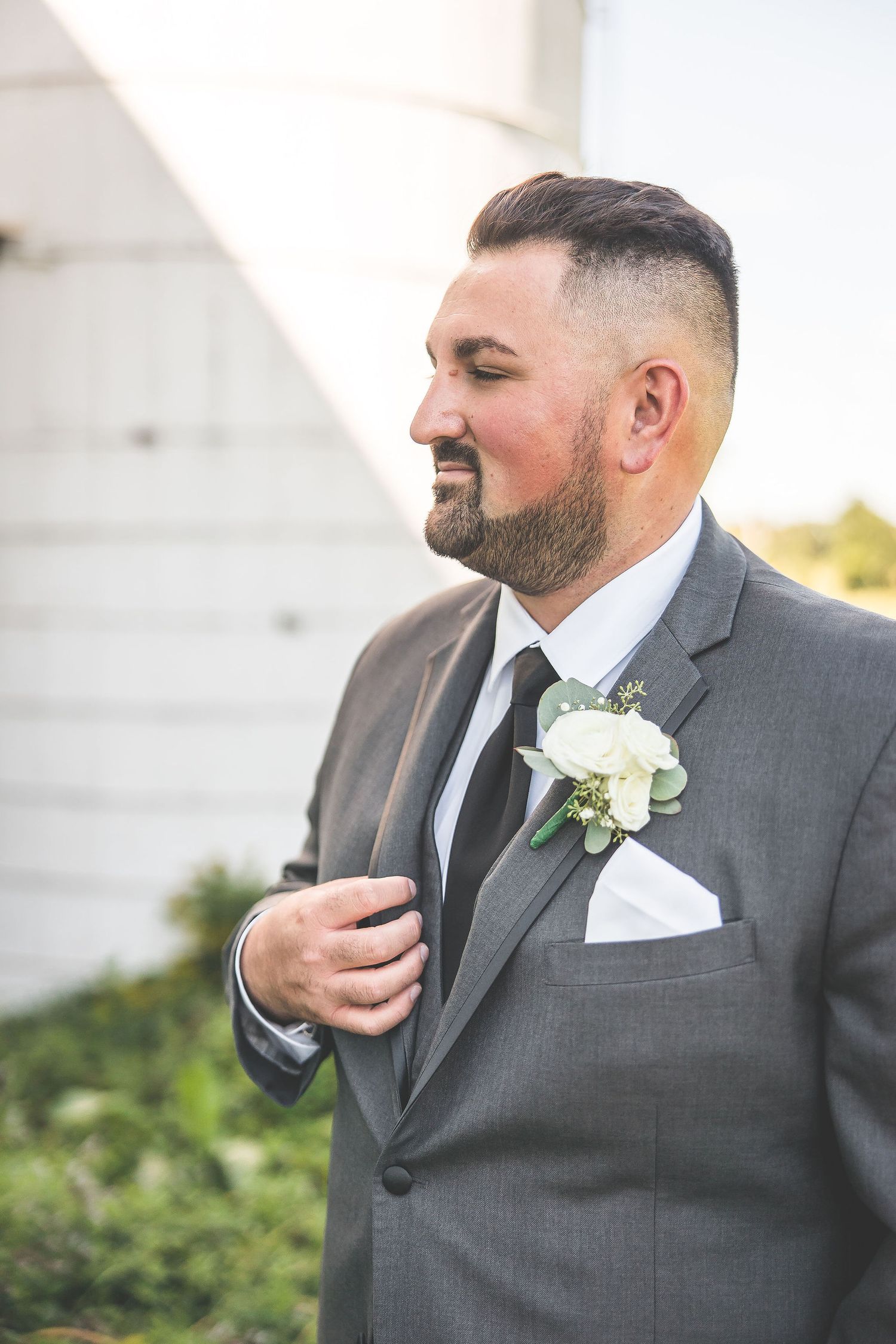 Close-up portrait of groom in grey suit with white boutonniere against white backdrop.