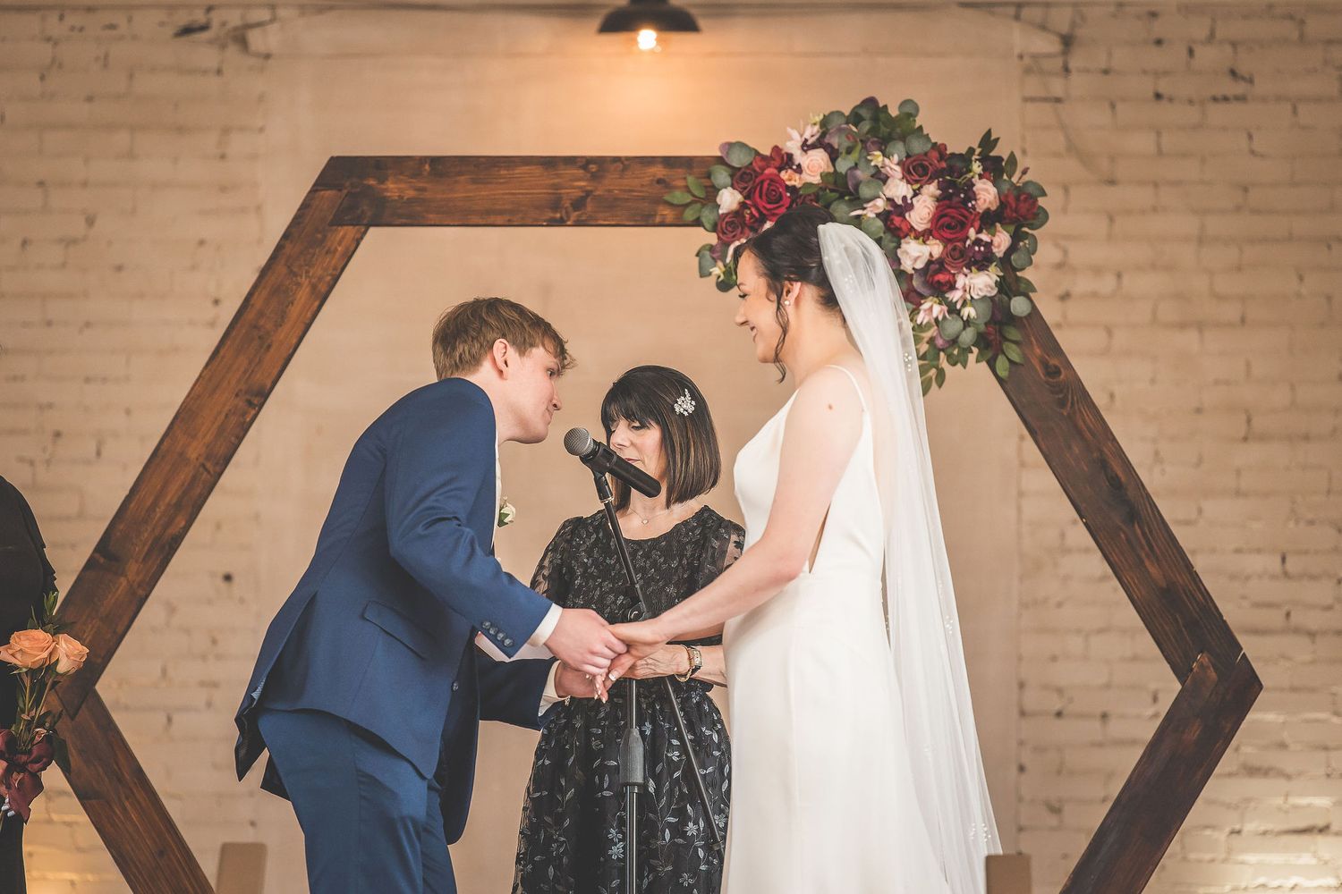 Wedding ceremony with wooden geometric arch decorated with pink and red flowers.