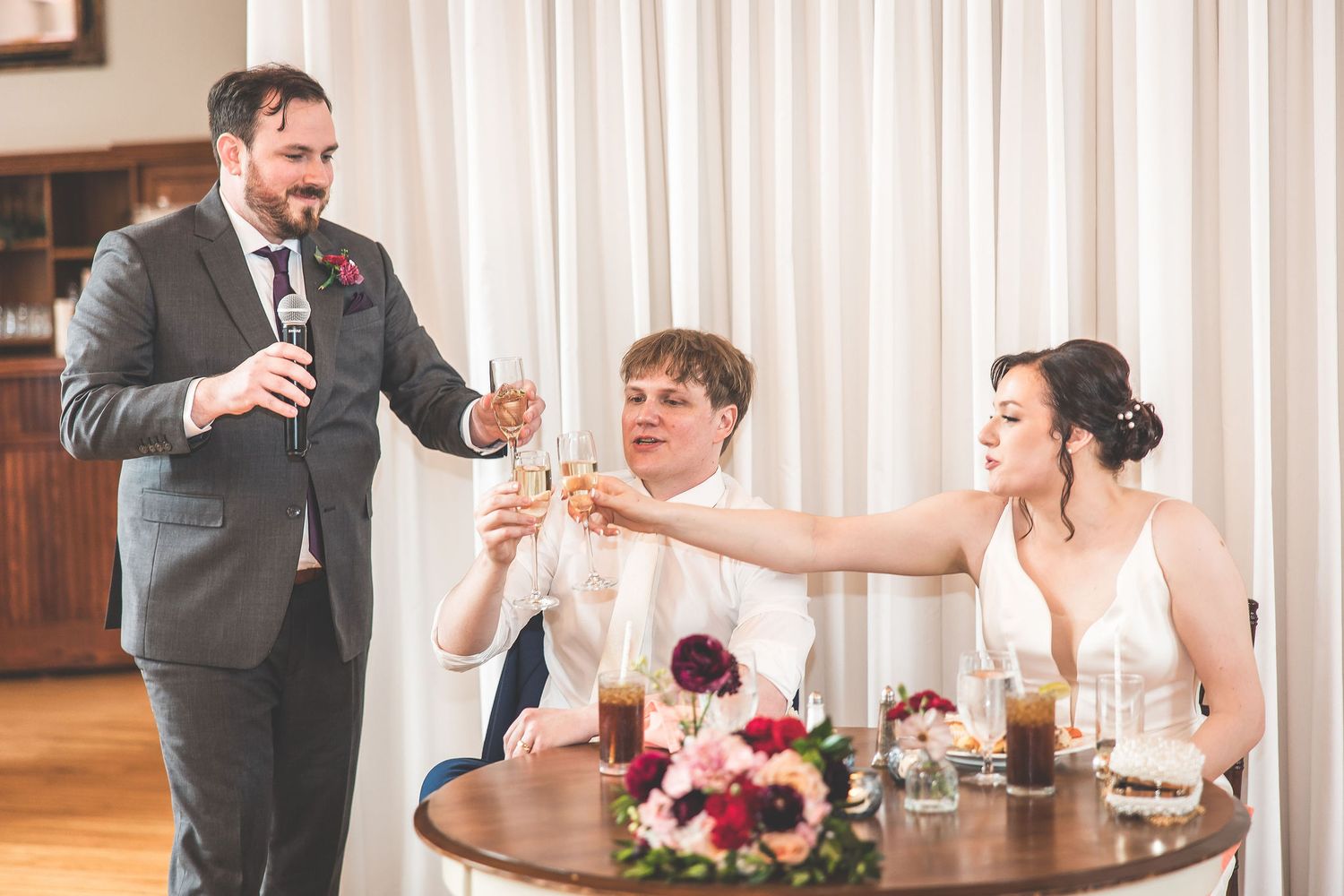 Candid moments captured during a wedding reception in an elegant venue with white drapery.