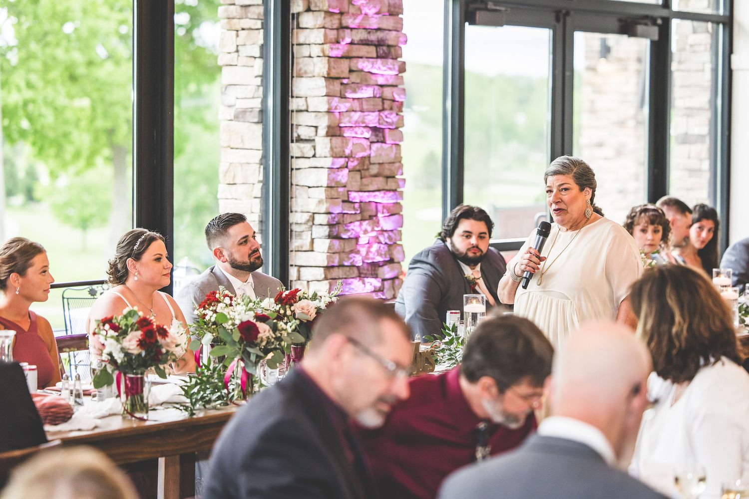Wedding reception table decorated with pink floral arrangements near large windows.