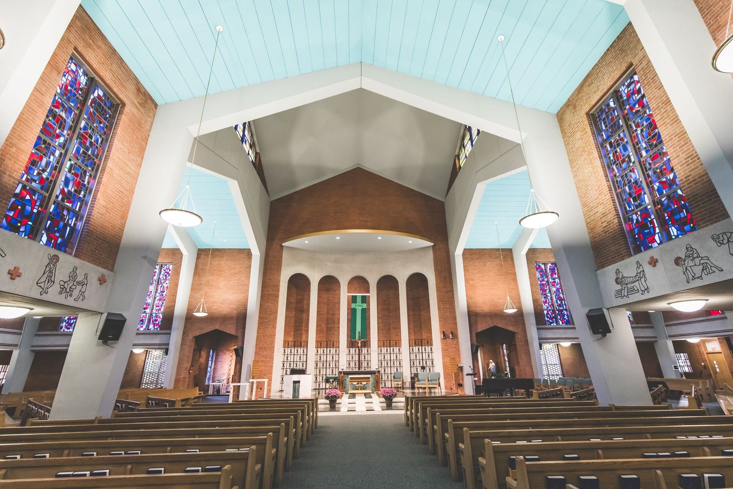 Interior view of a modern church sanctuary with stained glass windows and wooden pews leading to an altar.