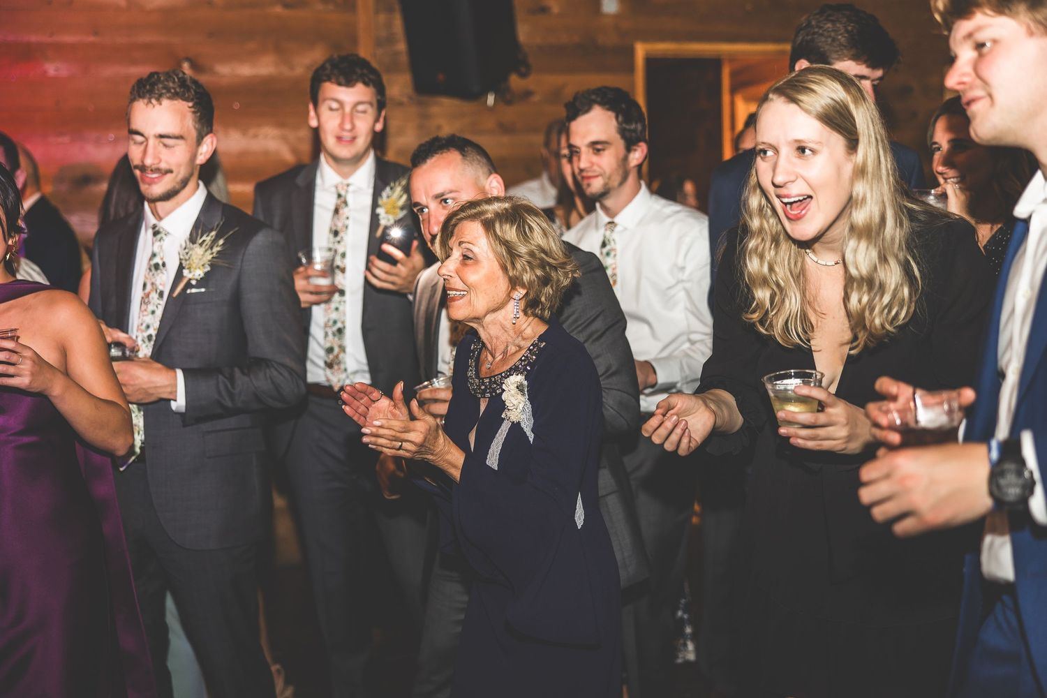 Guests celebrating and dancing during evening reception in wood-paneled venue with mood lighting.