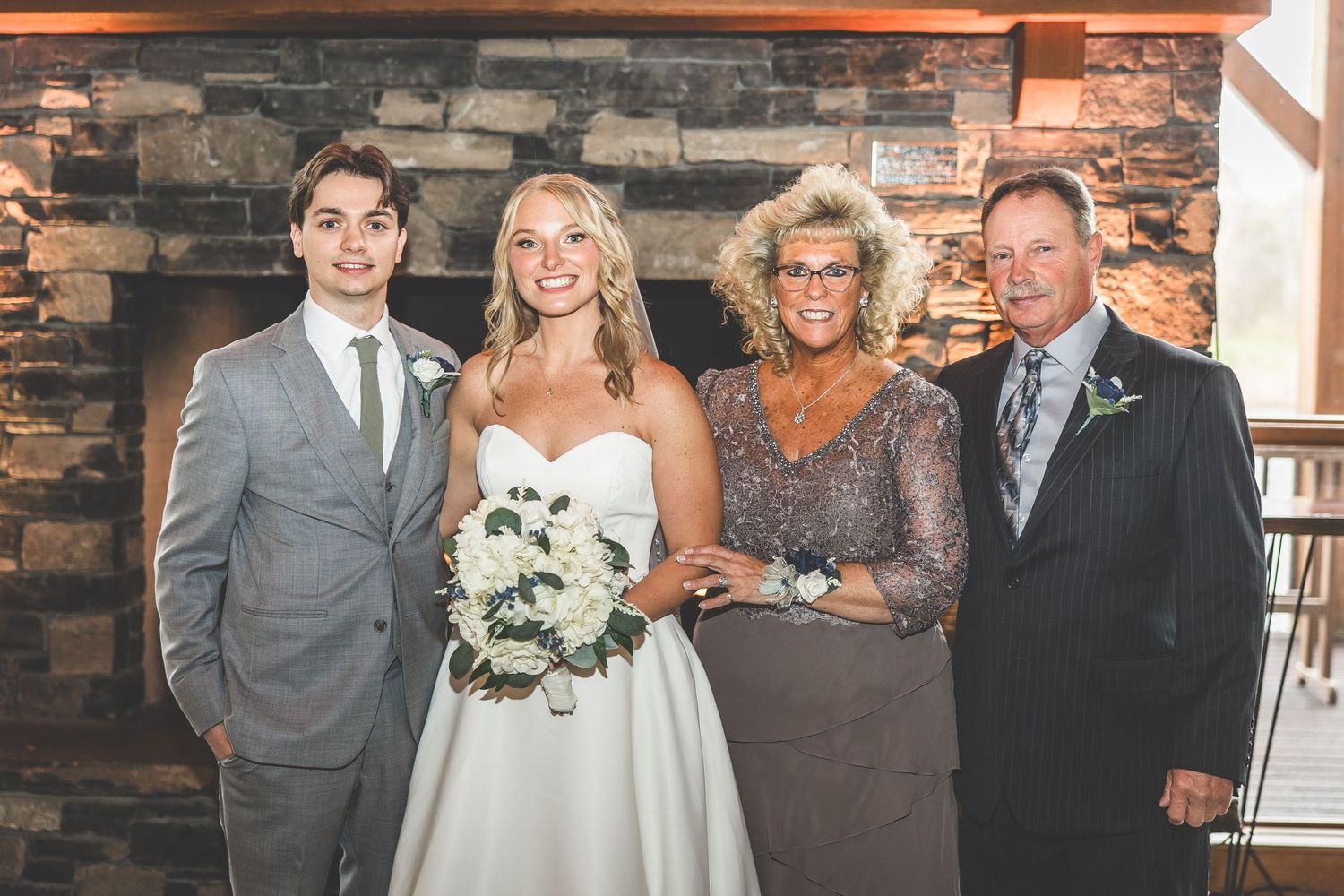 Wedding party members pose together against stone wall backdrop.