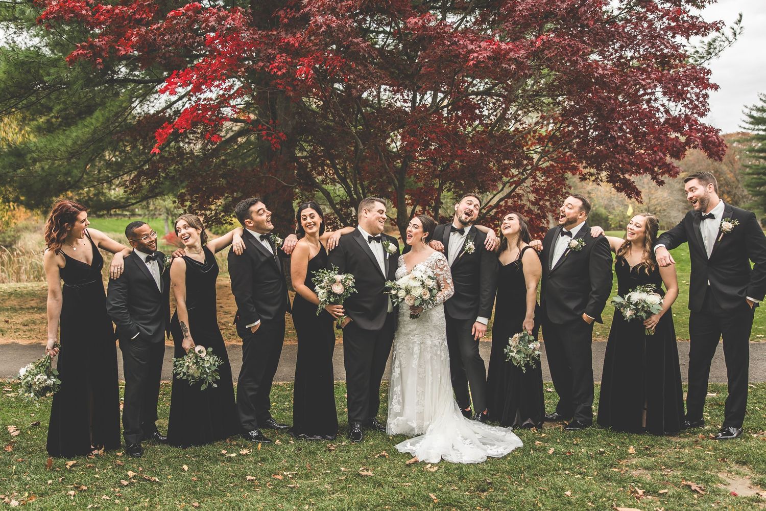 Wedding party lined up outdoors with stunning red maple tree backdrop in fall.