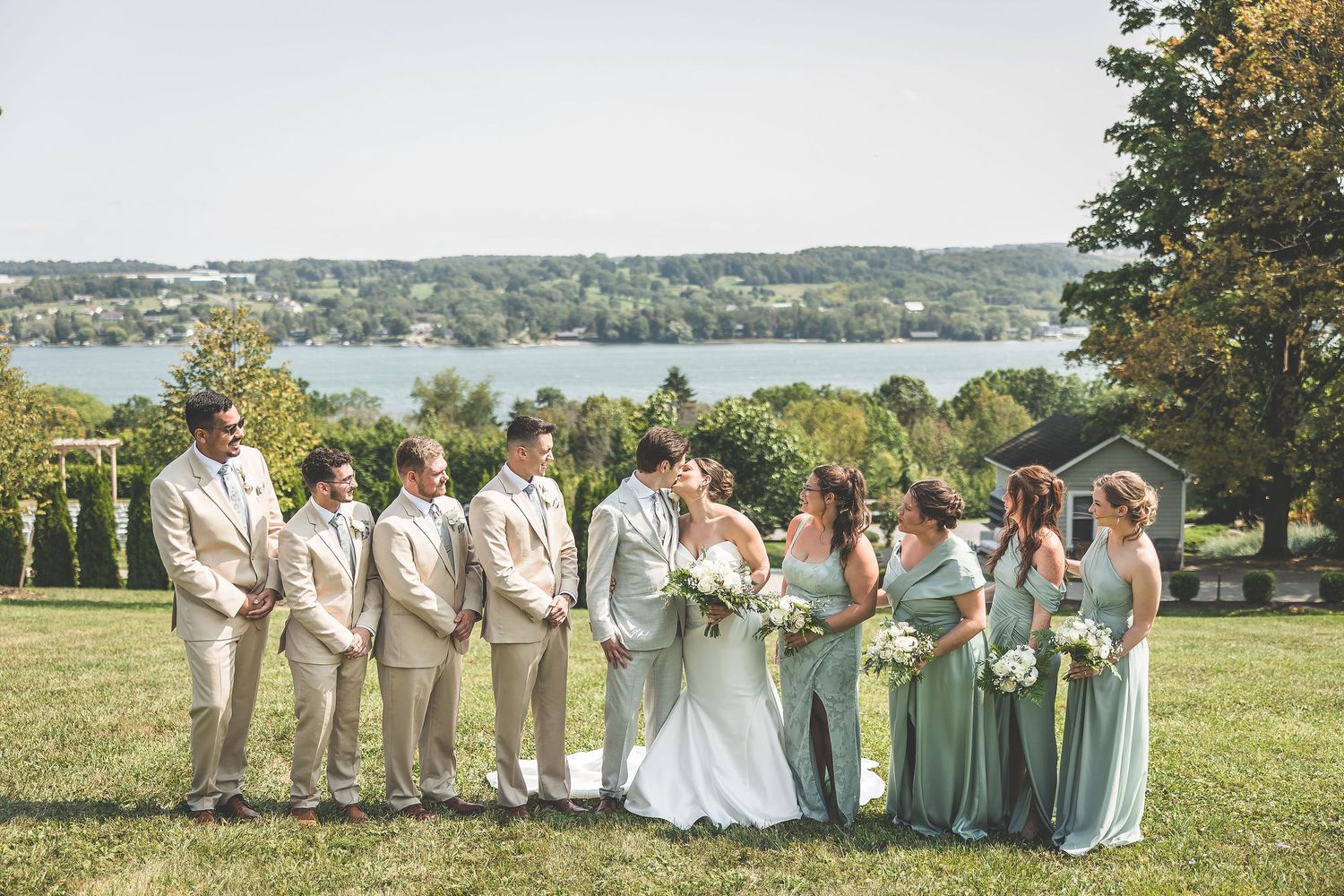 Wedding party arranged on a grassy hillside overlooking a scenic lake view.