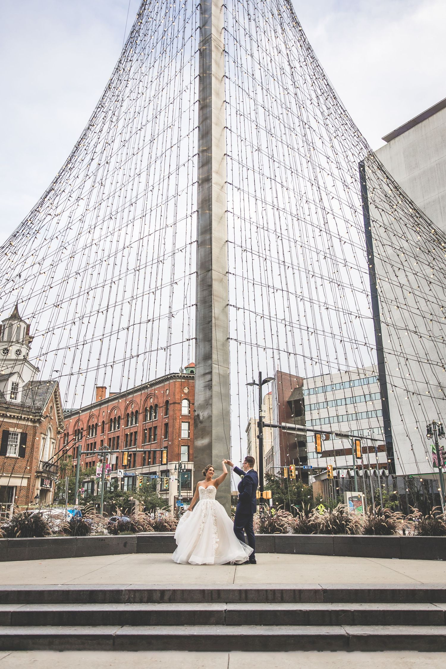 Wedding couple poses beneath large geometric glass structure in urban setting.
