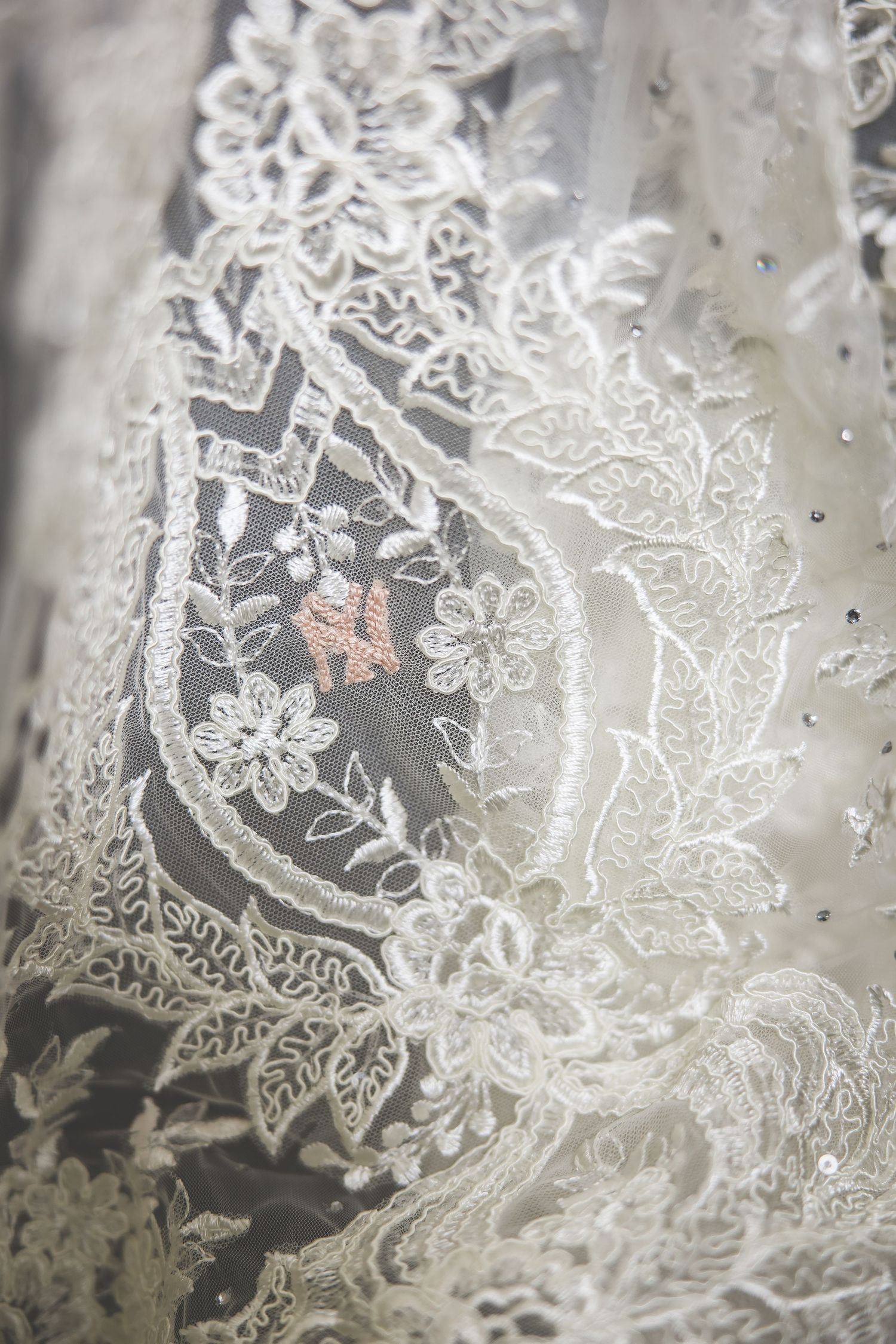 Close-up detail shot of intricate white lace pattern with floral designs on wedding dress fabric.