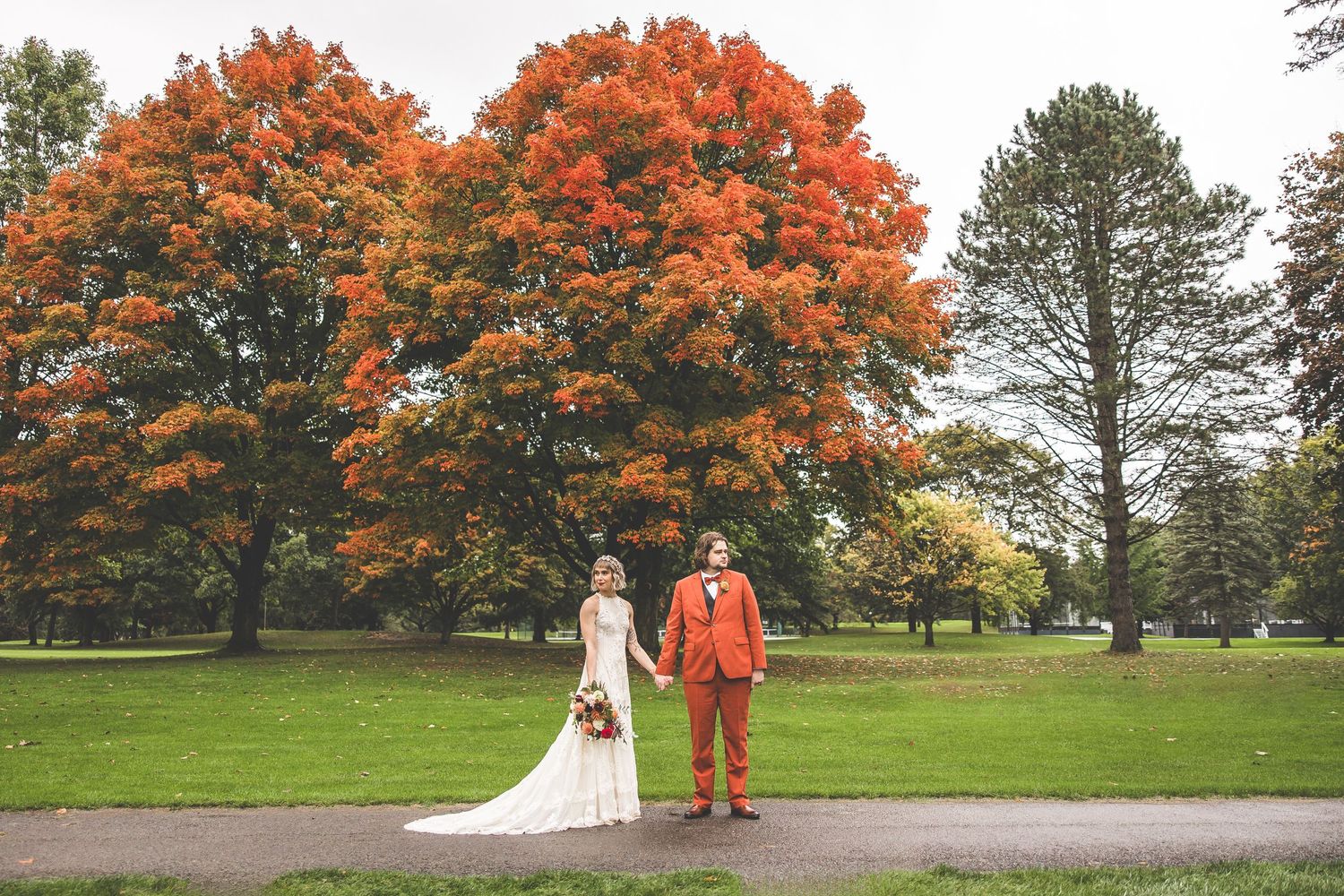 An autumn wedding photoshoot features a couple posing beneath vibrant orange maple trees.